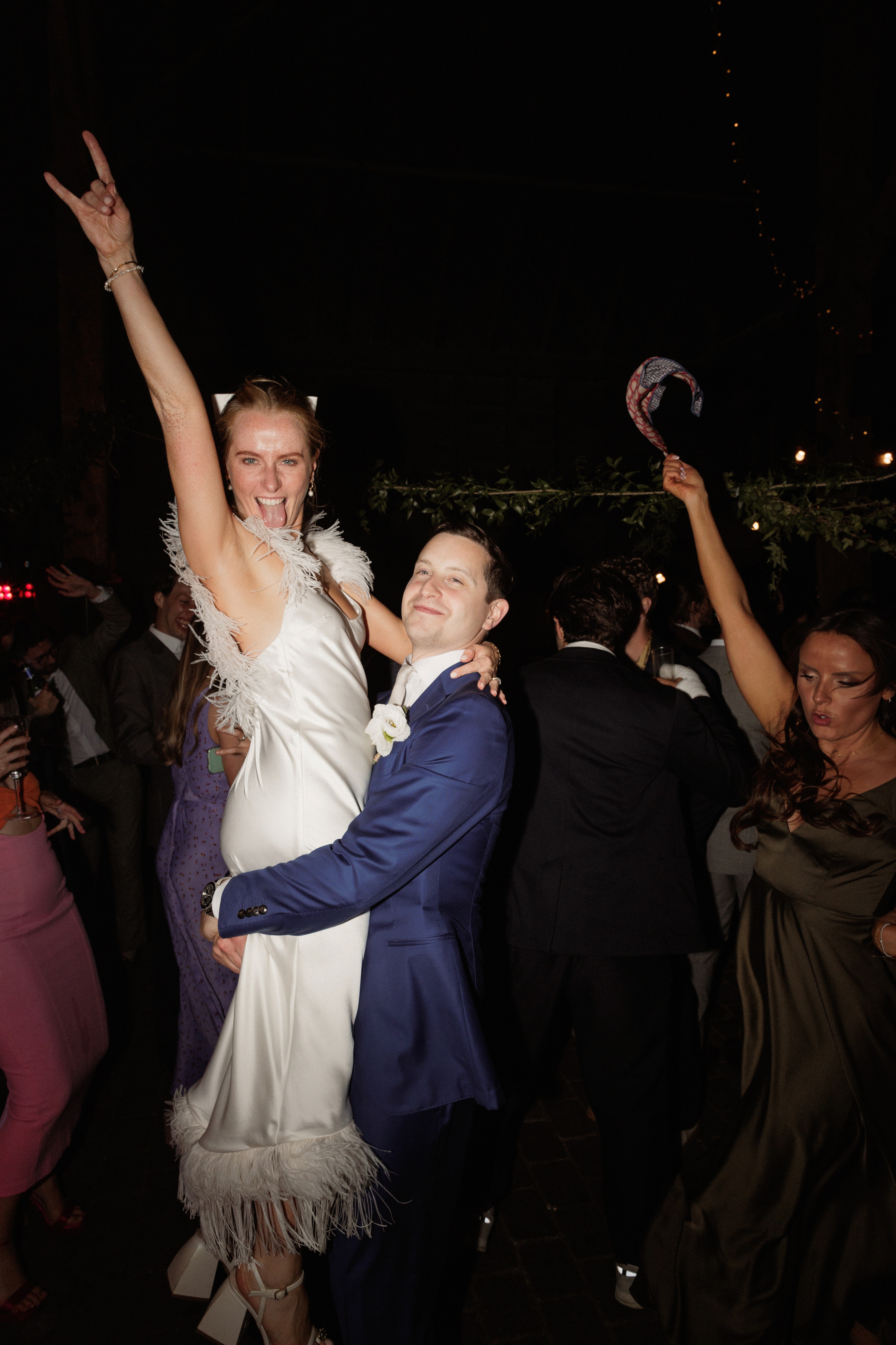 A Summer Wedding at Elmley Nature Reserve with Halfpenny London 111 Bride being lifted off the dancefloor in her ostrich feather Halfpenny London dress.