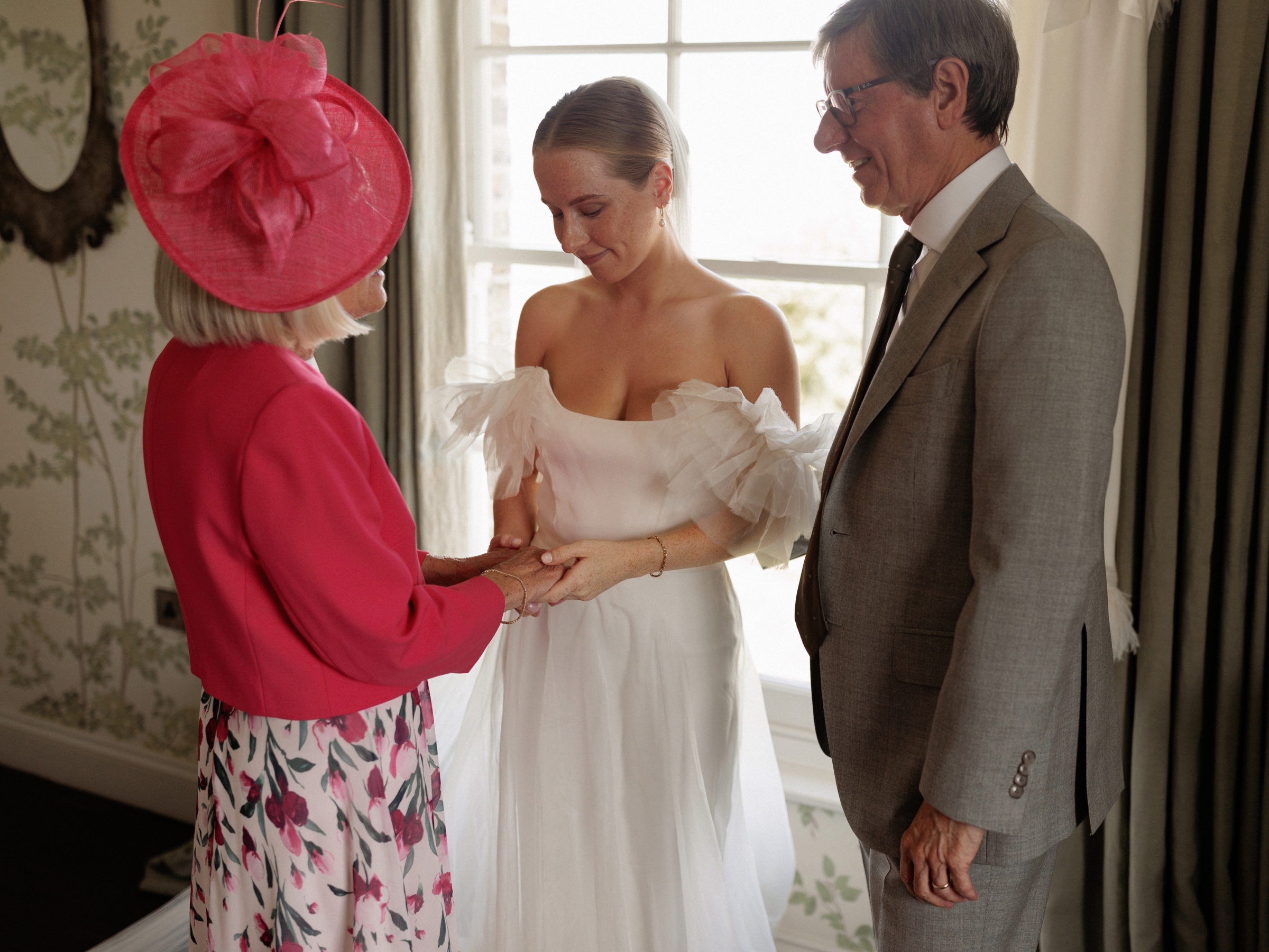 A Summer Wedding at Elmley Nature Reserve with Halfpenny London 46 Bride in a Halfpenny London dress with frilly sleeves and a long single tier veil. She is having. moment with her parents before the wedding ceremony.