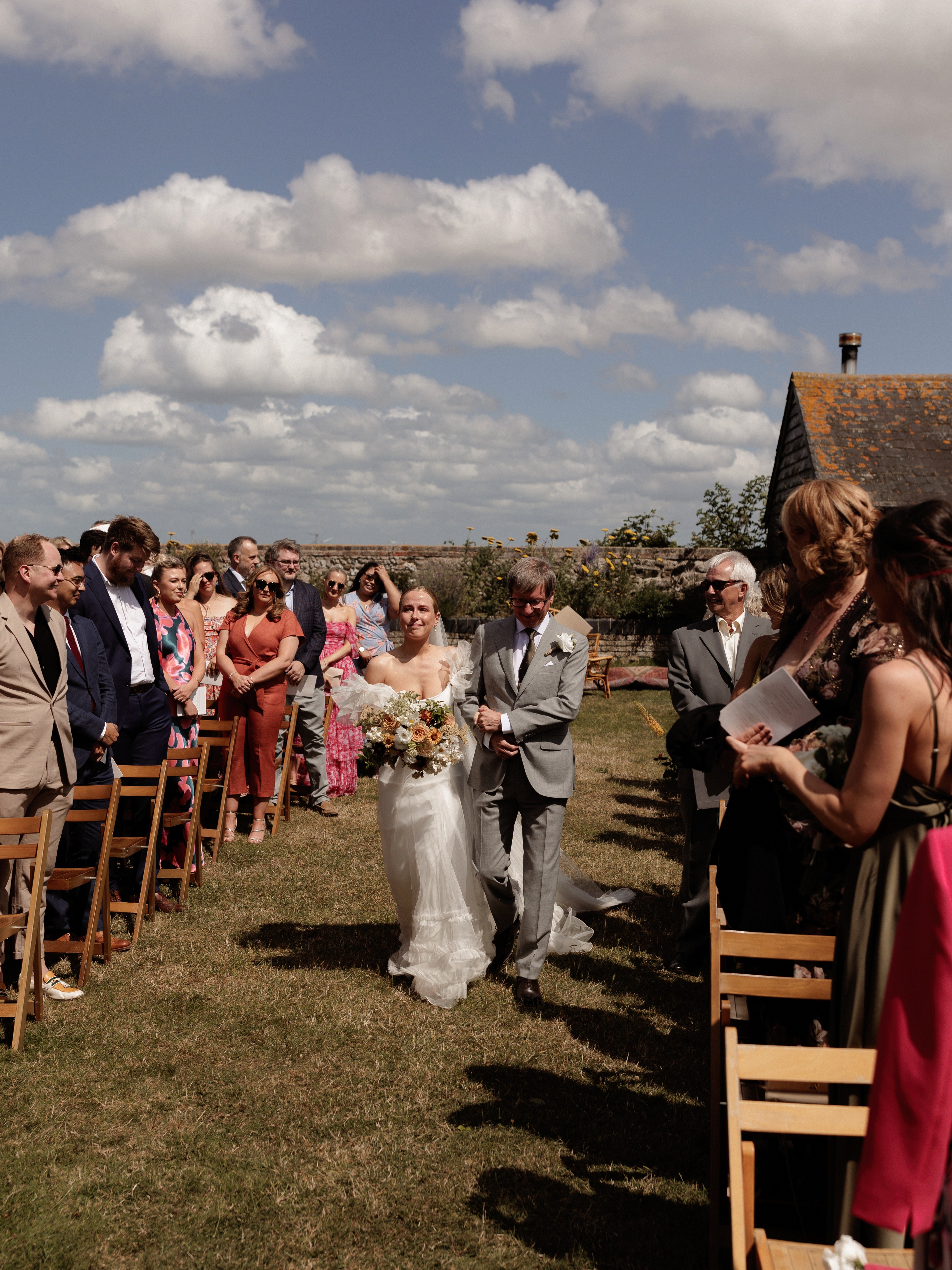 A Summer Wedding at Elmley Nature Reserve with Halfpenny London 51 Elmley Nature Reserve wedding - the bride is being accompanied by he father down the aisle.