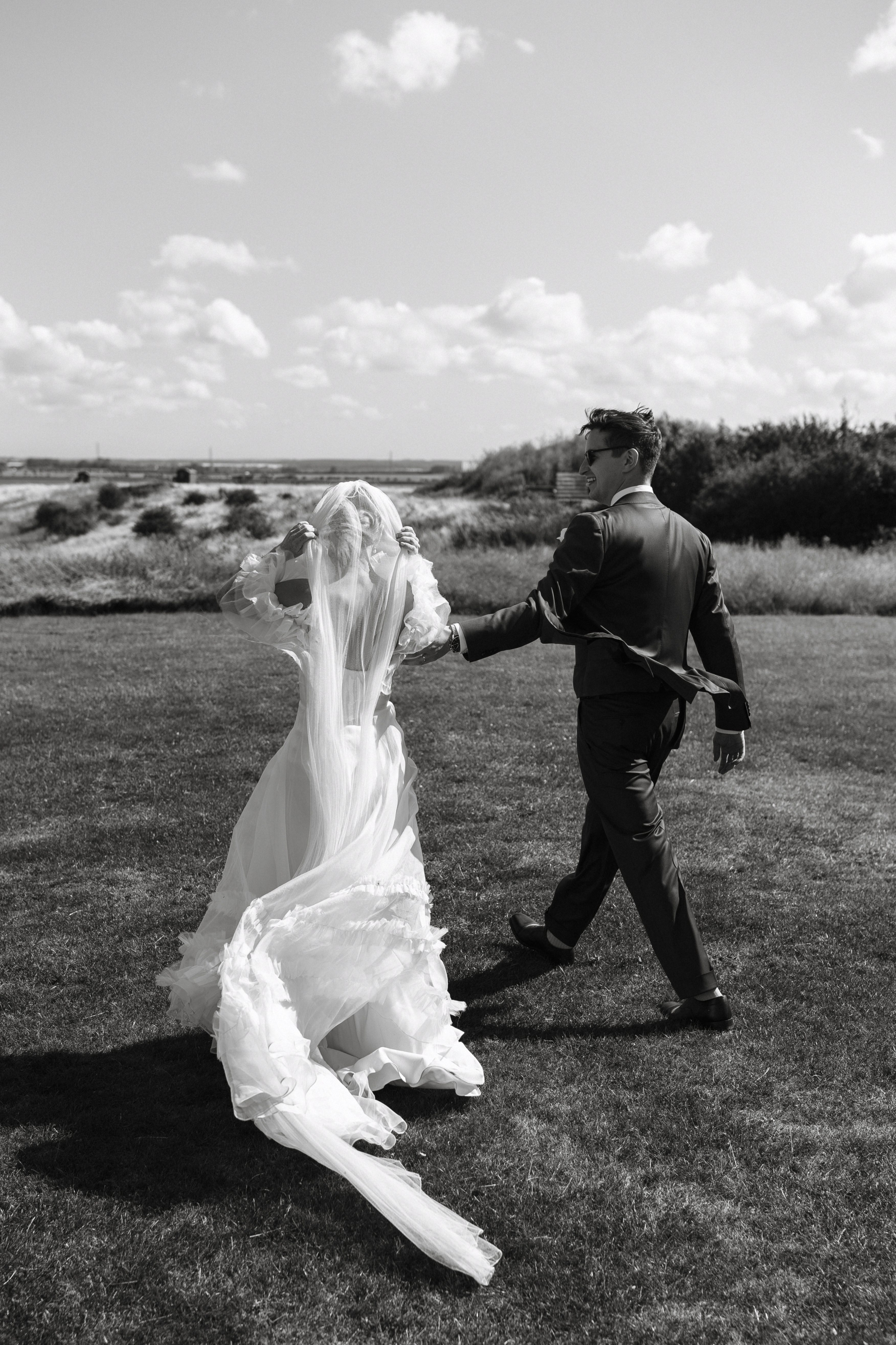 A Summer Wedding at Elmley Nature Reserve with Halfpenny London 58 Bride holding on to her veil during a windy moment at Elmley Nature Reserve wedding venue in Kent.