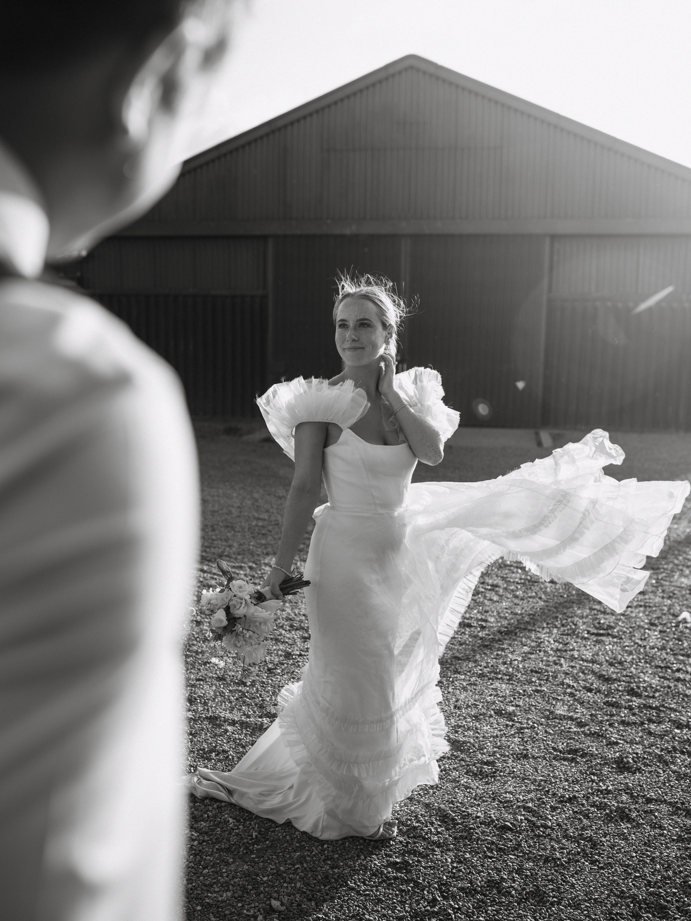 A Summer Wedding at Elmley Nature Reserve with Halfpenny London 101 Black and white golden hour wedding photography at Elmley Nature Reserve in Kent. Bride is wearing a Halfpenny London dress that is caught in the breeze.