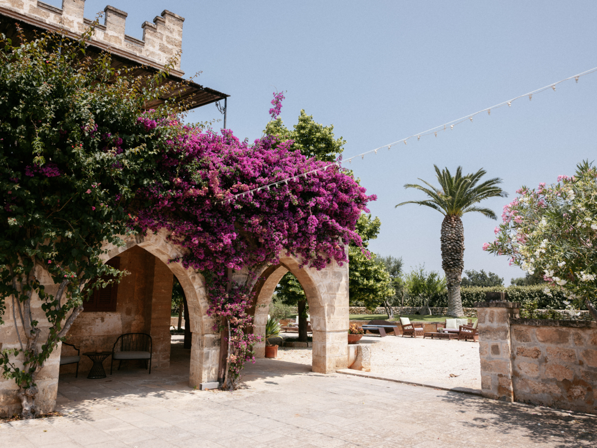 Will & Heather's Romantic Wedding in Puglia Inspired by Classic Italian Design 38 Masseria Salamina wedding venue in Puglia Italy. Beautiful stone building covered in pink flowers and surrounded by palm trees.
