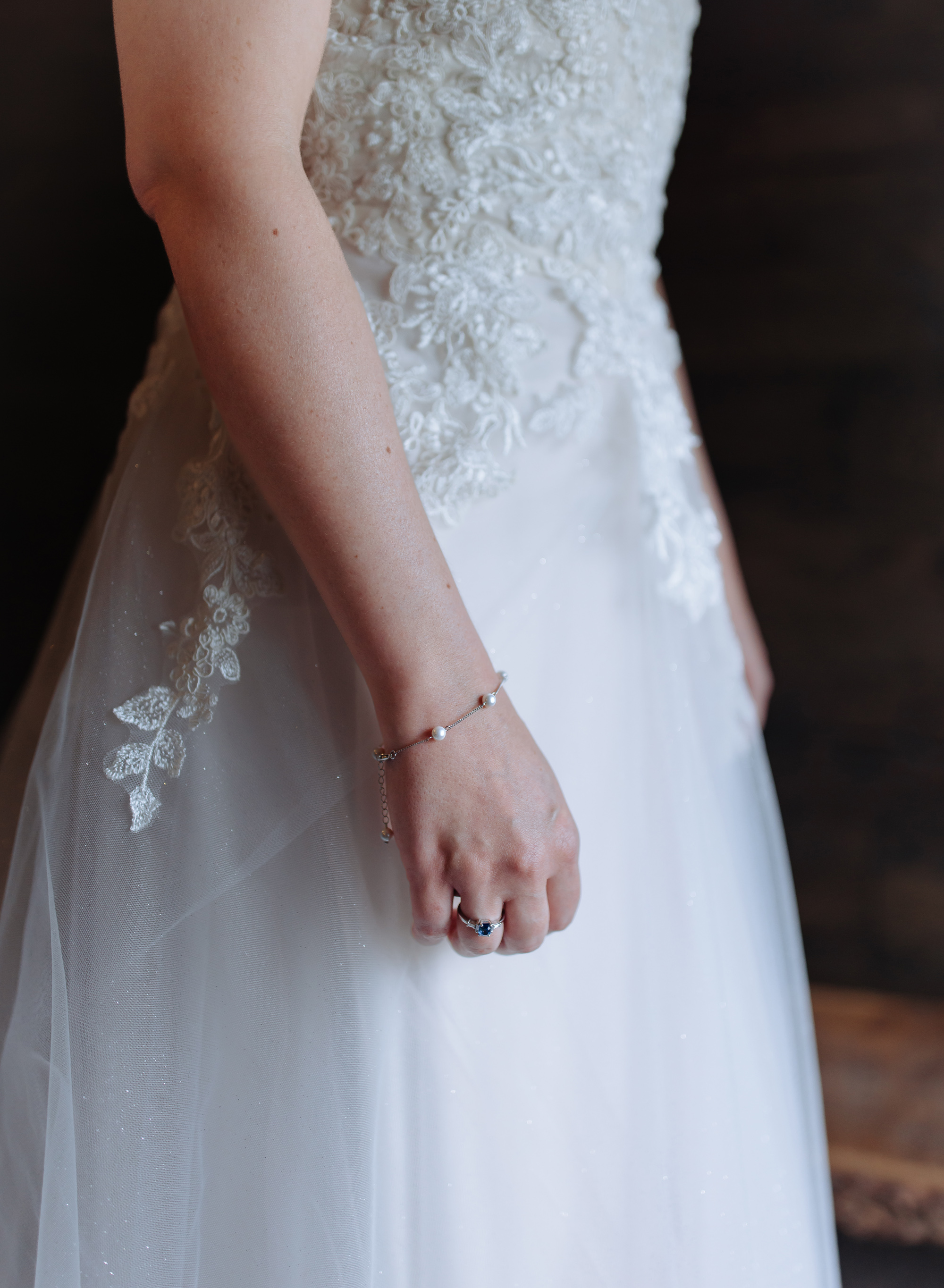 Close up of a bride's tulle and lace dress - she wears a delicate gold and pearl bracelet.