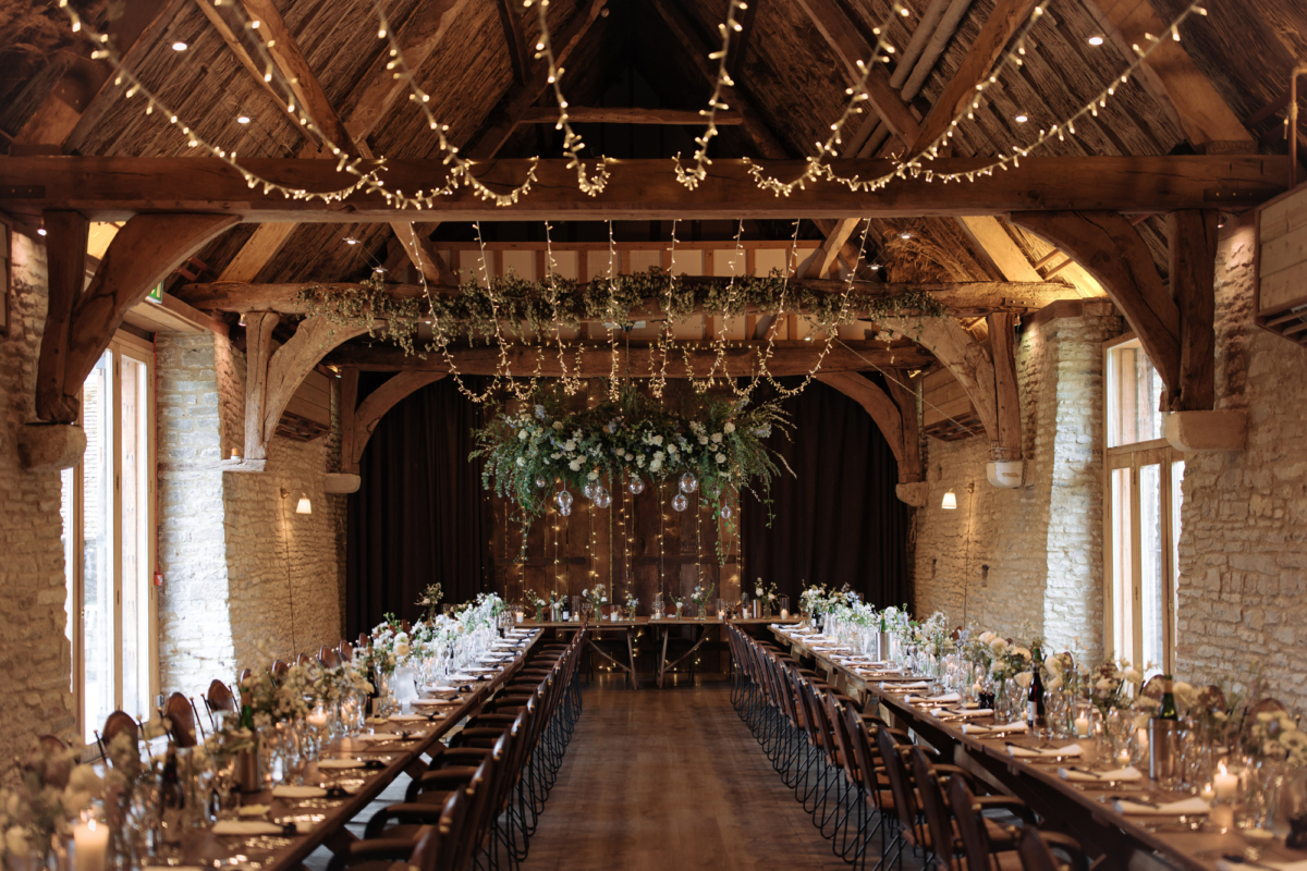 Tythe, Oxfordshire ban wedding venue, with long trestle tables, fairylights and hanging greenery.