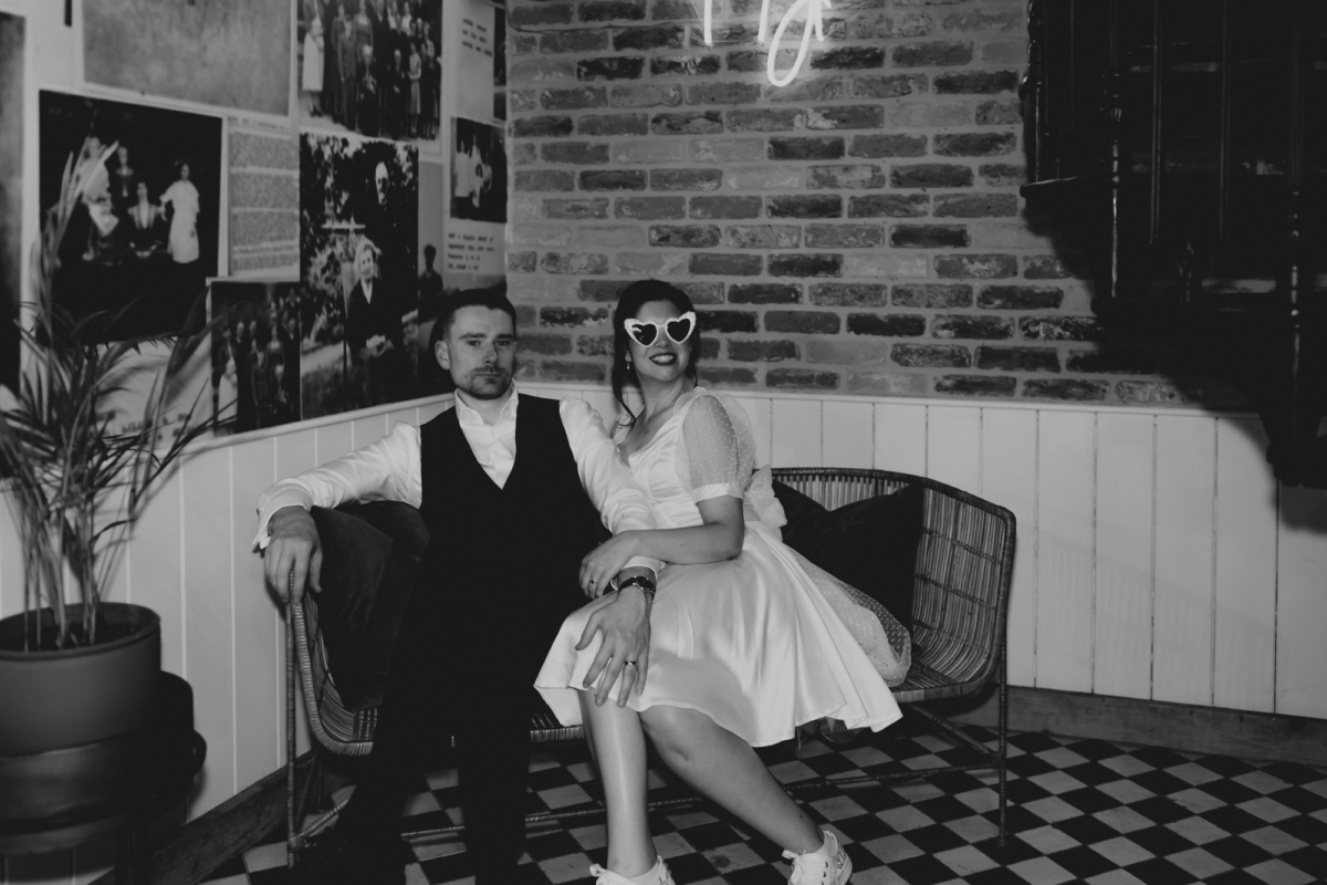Bride wearing heart shaped sunglasses and a short evening dress and trainers for her wedding at Tythe, an Oxfordshire barn wedding venue.