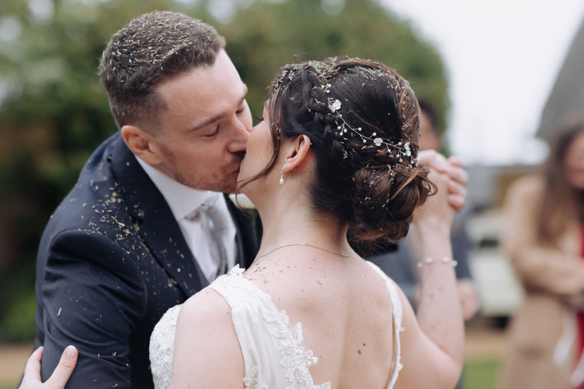 Bride and groom embracing and kissing, they ave been showered in flower seeds as confetti.