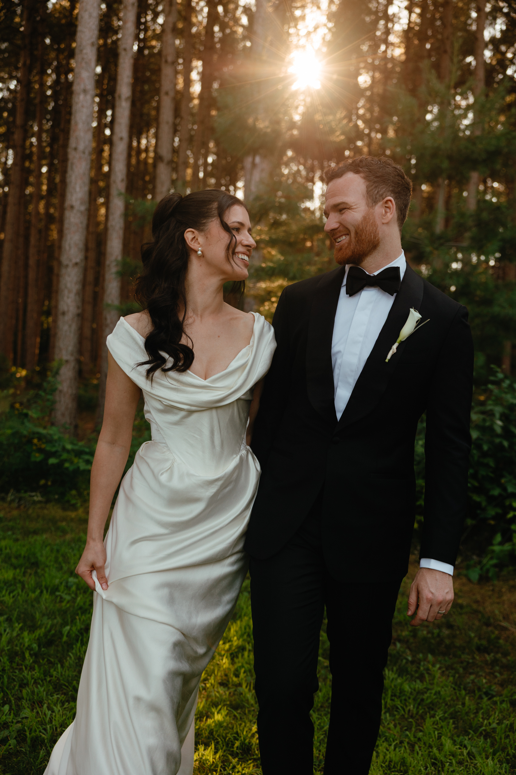Bride in Vivienne Westwood and groom in black tie. They are standing in the middle of a forrest with the sunshining through the trees.