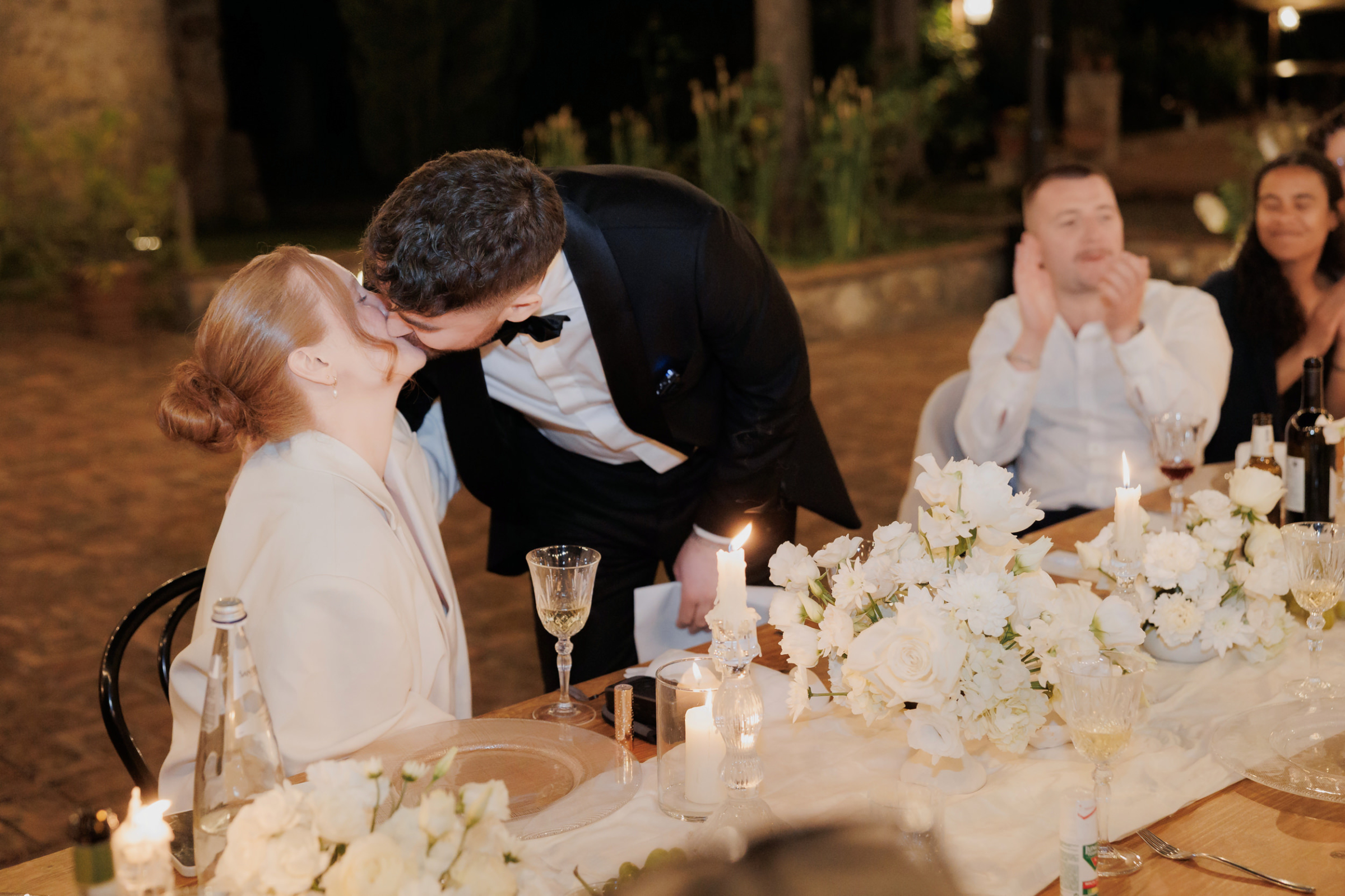 An Arakii Suit with Oversized Jacket for a Chic Italian Wedding at Antico Borgo 84 Groom leaning in to kiss his seated bride. Wedding at Antico Borgo San Lorenzo in Poggibonsi, Italy.