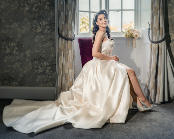 Elegant bride seated by the window in satin gown - fine-art wedding portrait by Calini Weddings.