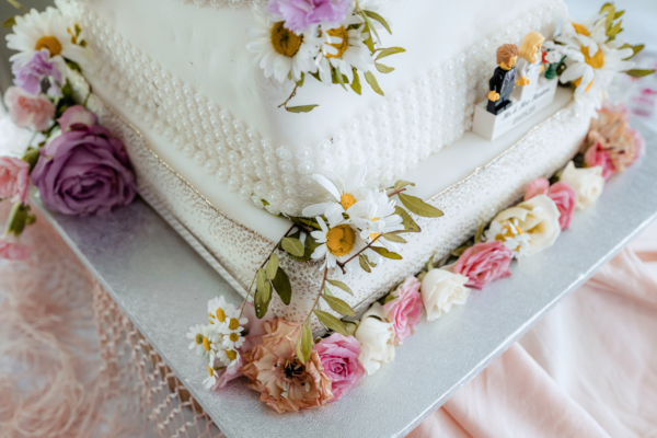 Floral-decorated white wedding cake with daisies and roses - elegant detail photograph by Calini Weddings.