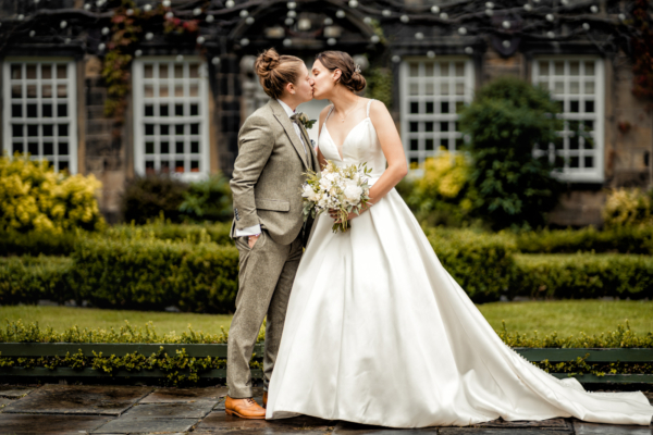 LGBTQ wedding couple kissing in elegant garden setting – inclusive fine-art photography by Calini Weddings.
