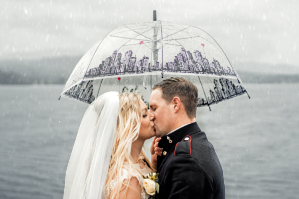 Bride and groom kissing under umbrella in rain - romantic Lake District wedding photography by Calini Weddings.