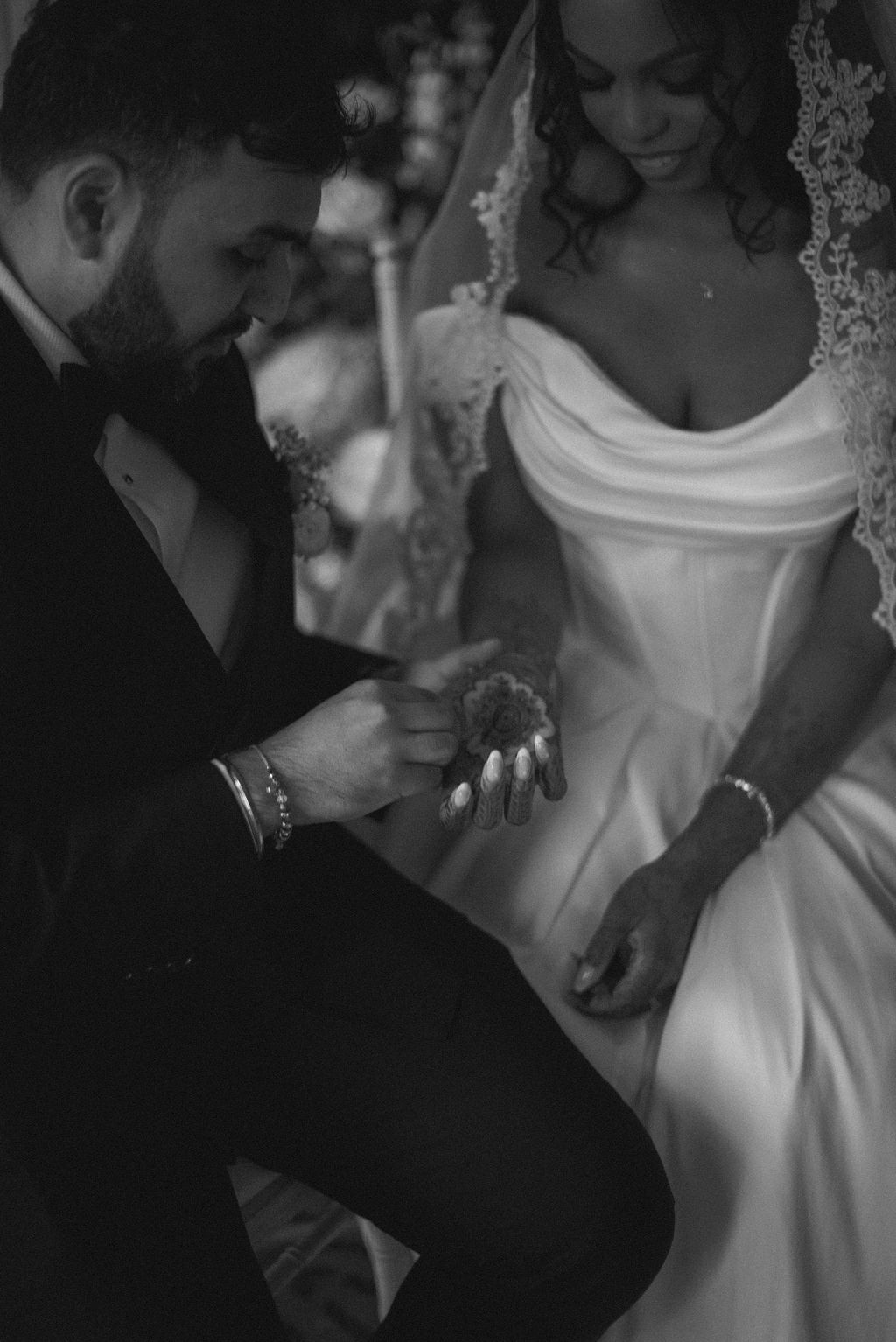 Tender black and white shot of a groom gently holding his bride's hands as he admires her henna tattoos.