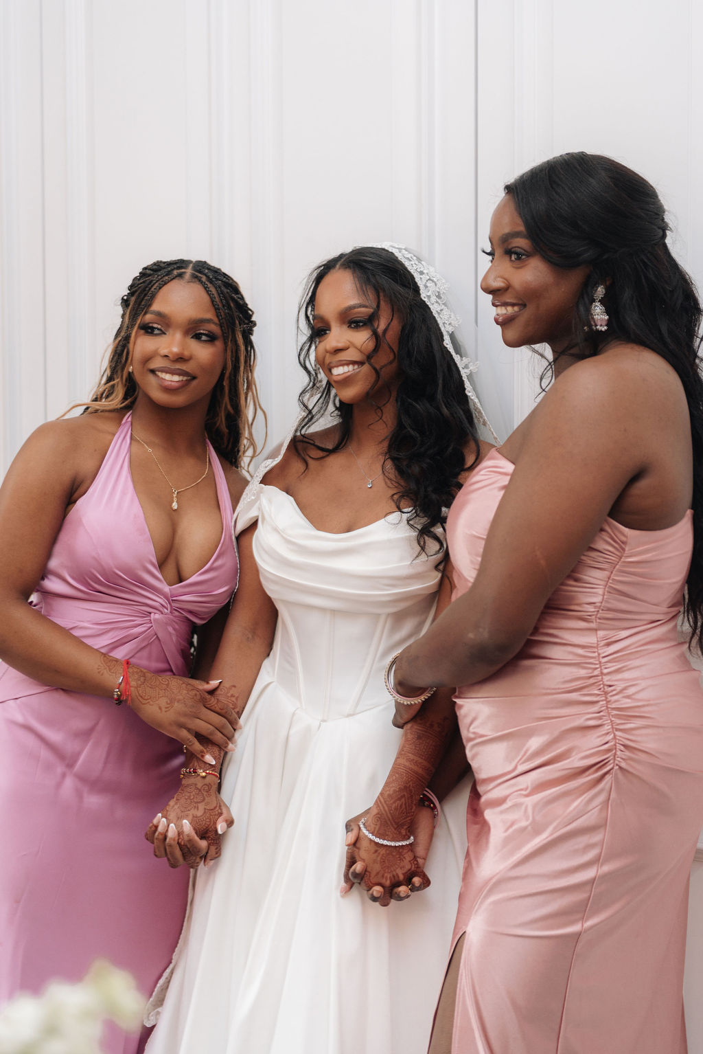 Bridesmaids in pink dresses holding the arms of the bride.