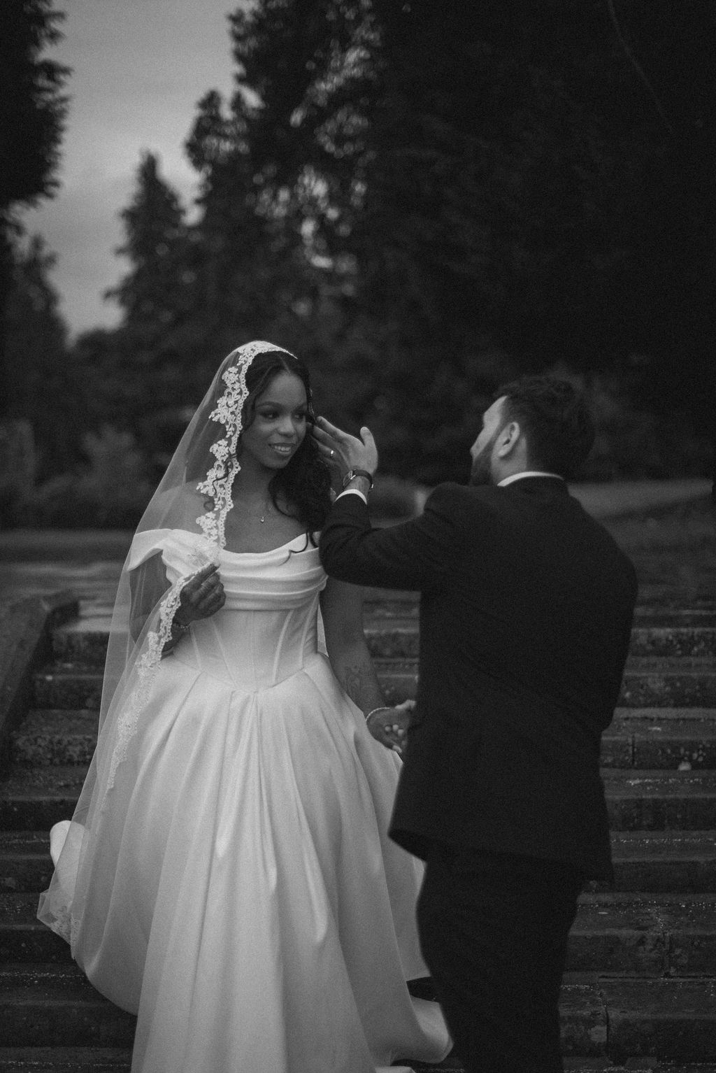 Tender black. and white wedding photography of Groom gently pulling his bride's veil away form her face. 