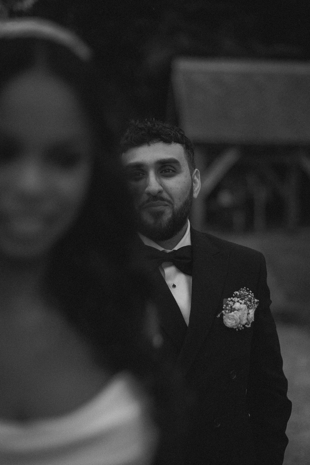 Tender black. and white wedding photography of Groom in black tie looking lovingly at his bride ahead of him.