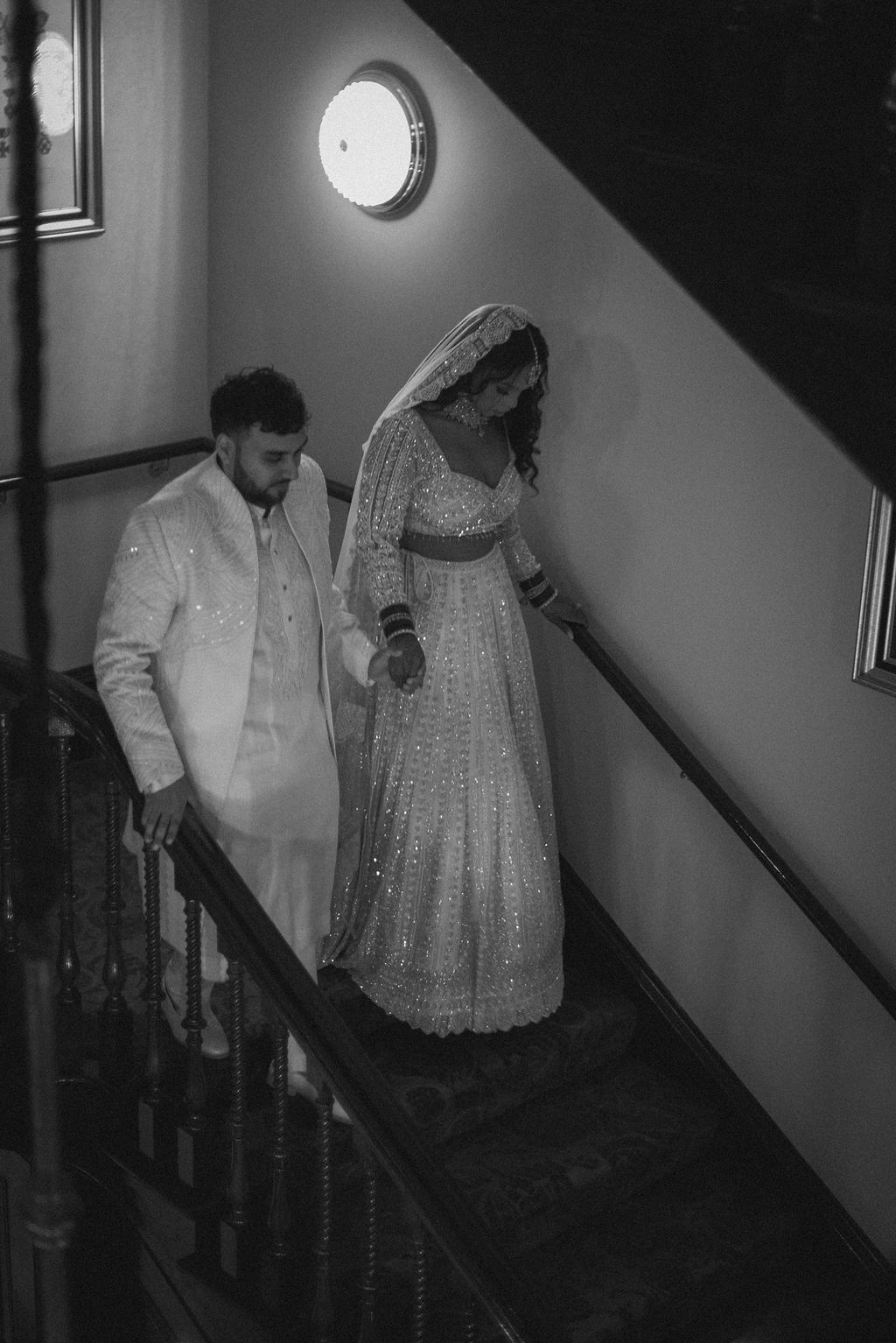 Elegant black and white wedding photography of Indian groom in traditional white sherwani and a bride in a sparkly lehenga with a sparkly lace mantilla veil.