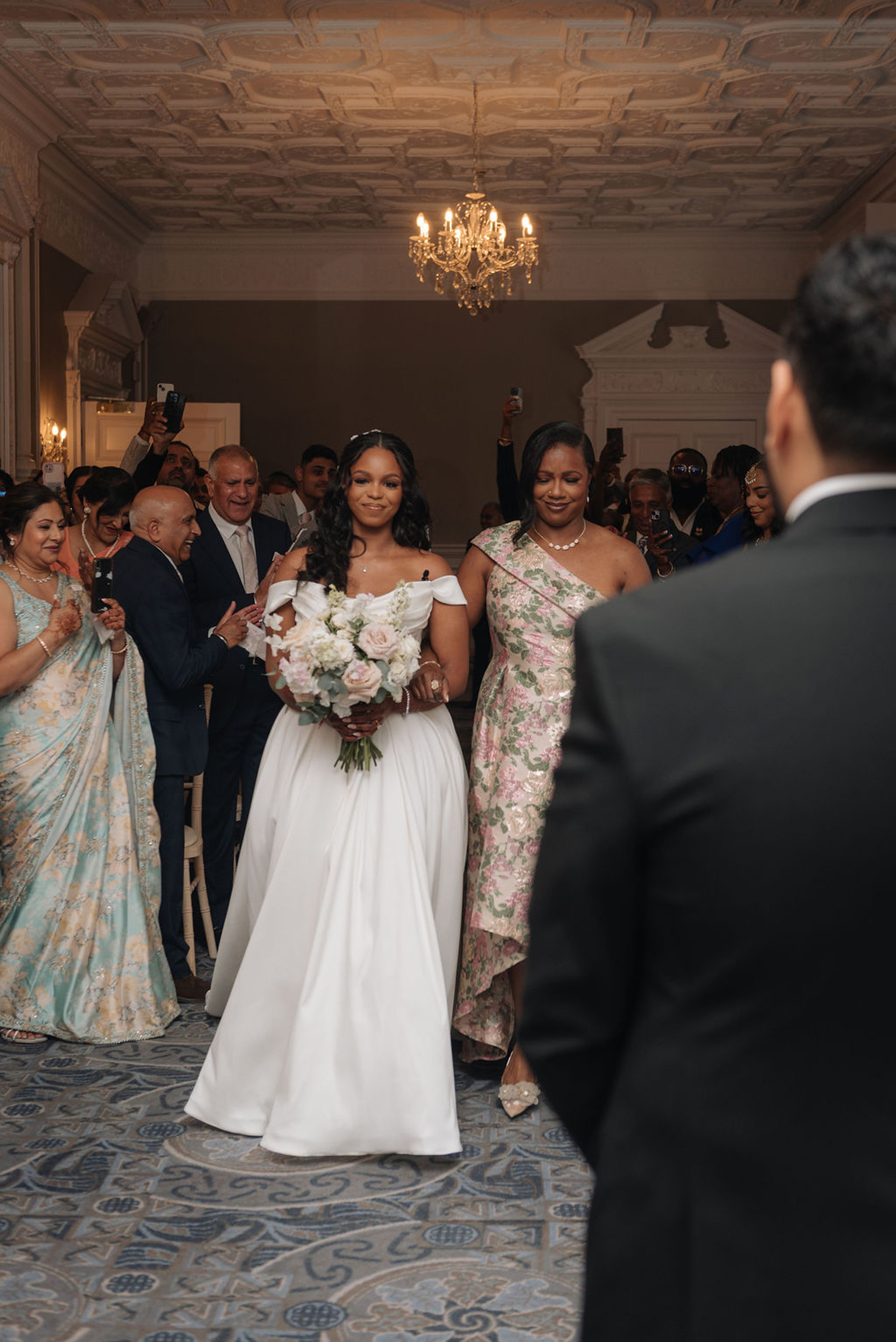 Bride and groom newlywed leaving their multicultural wedding ceremony at Oakley Hall. they both wear pale pink and white floral garlands around their necks.