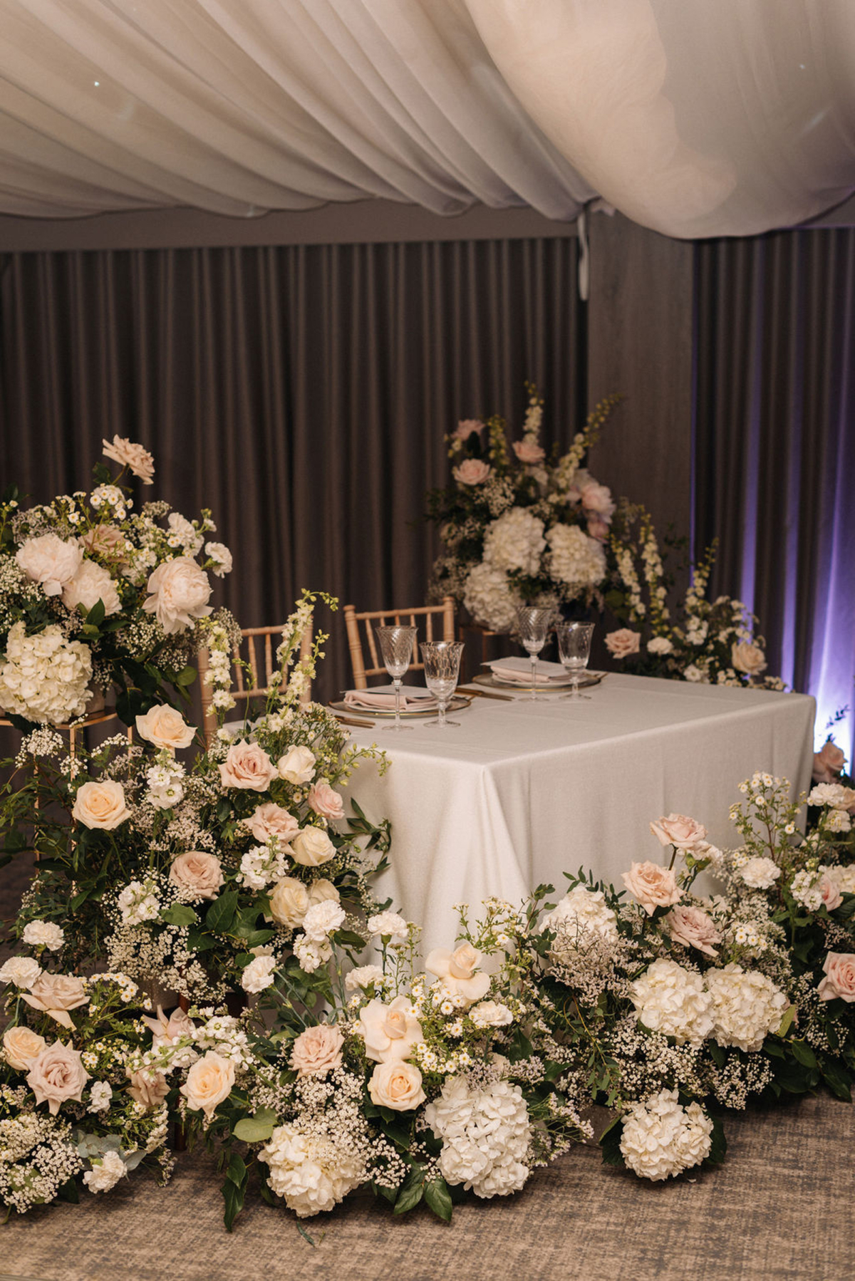 Wedding sweetheart table surrounded by pale peach and pink roses, hydrangea and 