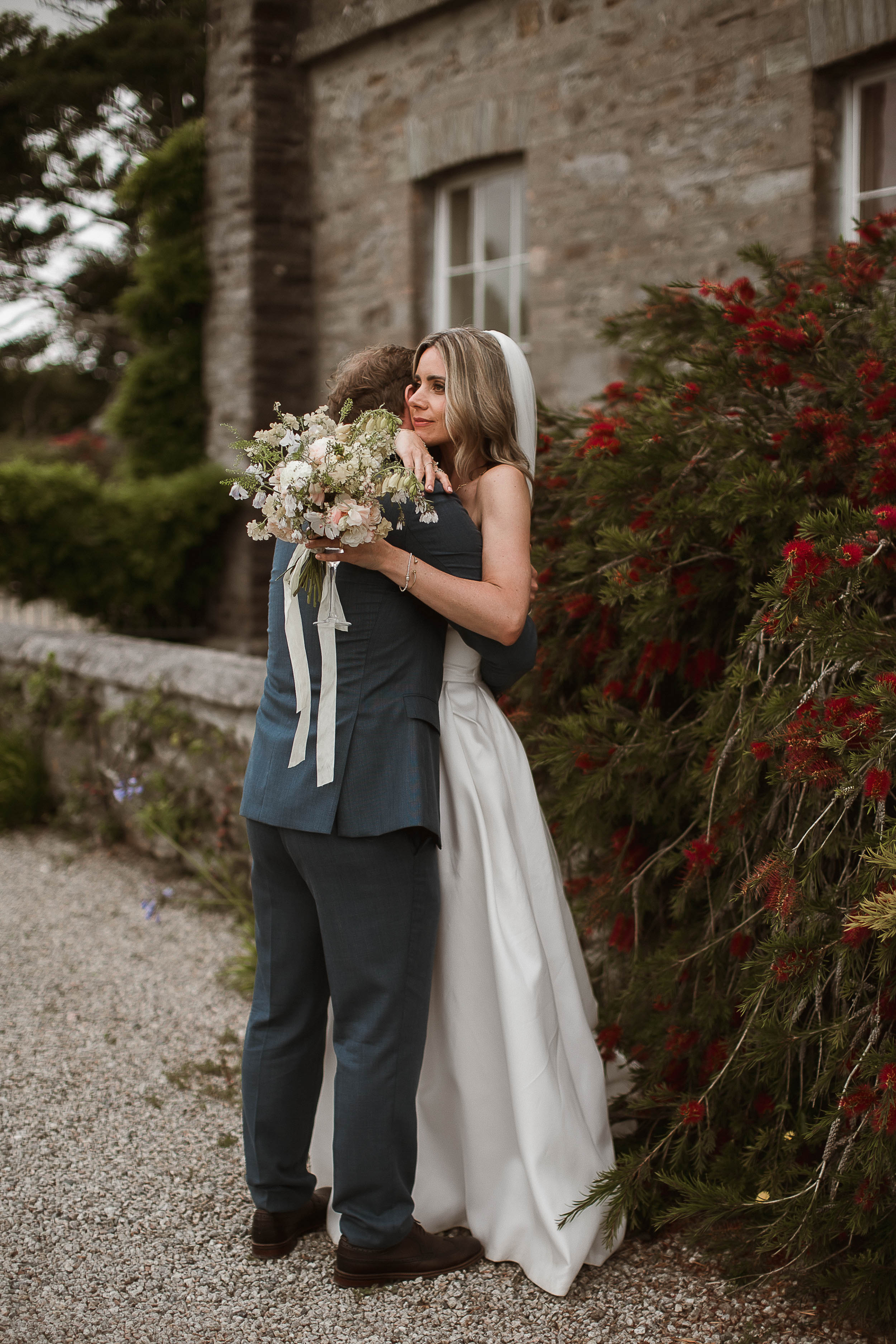 Boconnoc Estate Wedding Cornwall Jesus Peiro 144 - Lauren in Jesus Peiro for her Elegant Boconnoc Estate Wedding in Cornwall Bride and groom hugging outside of Boconnoc Estate house. She carries a beautiful and elegant summer bouquet with Foxgloves.