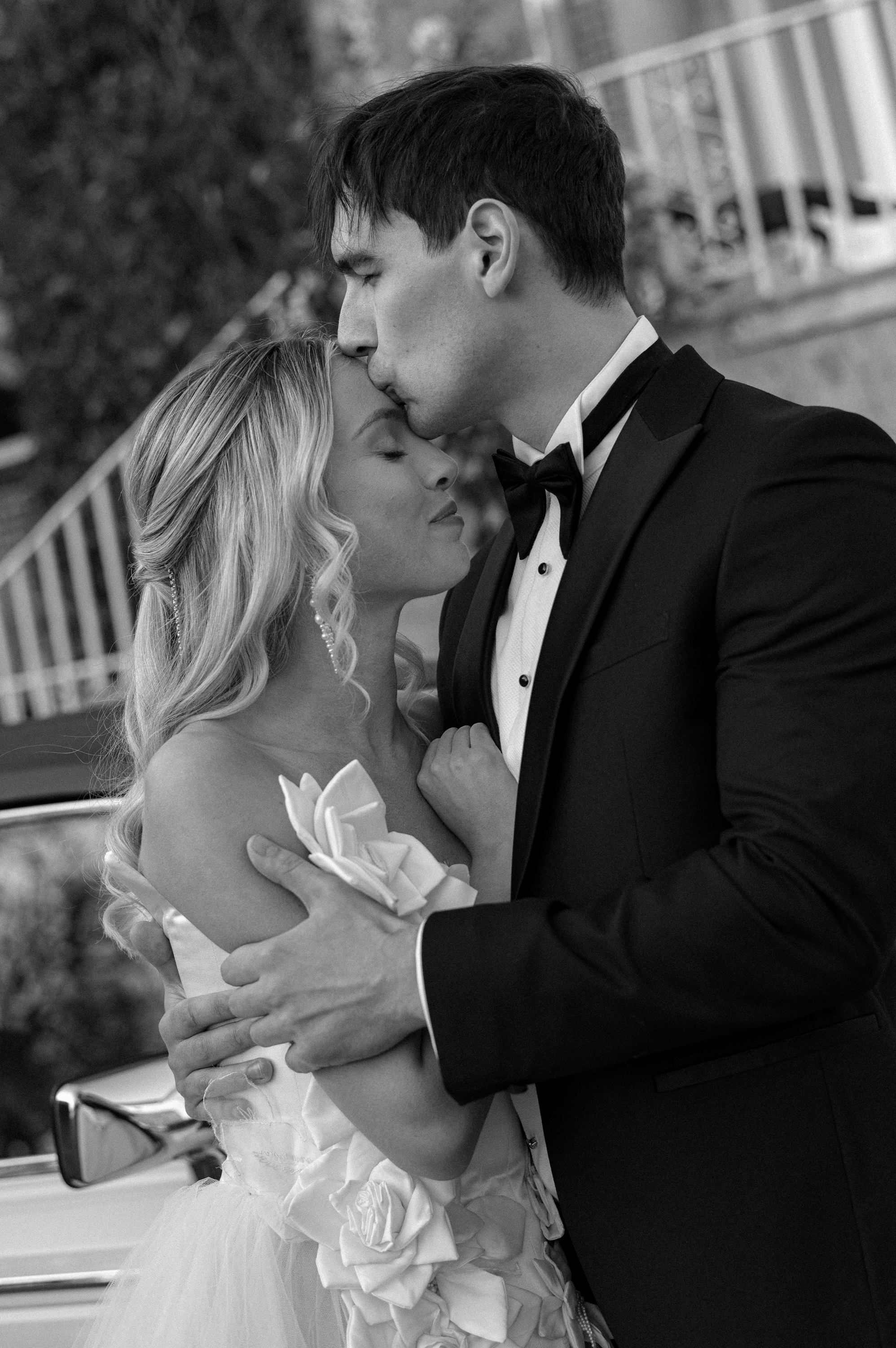 Earnshill House Wedding Editorial Fern Godfrey Weddings 11 - Modern Bridal Elegance at Earnshill House, A Romantic Somerset Wedding Venue Groom in black tie embracing a bride wearing a JULITA dress that features 3D silk roses. Earnshill House, A romantic Somerset county house wedding venue.