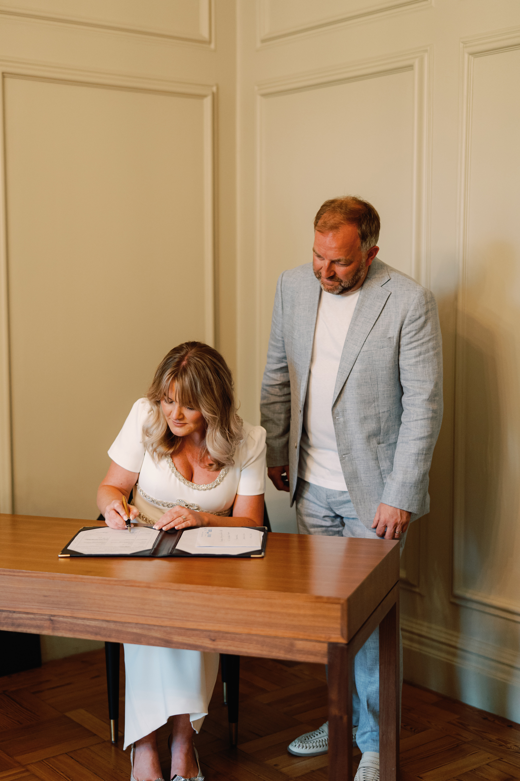 Emmylou Kelly Registry Office Wedding Jessica Lily Photography 109 - Photographer Emmylou Kelly & Paul's Intimate Family Registry Office Wedding Bride and groom signing the register during their ceremony at Old Marylebone Town Hall. She carries a small bouquet of Chamomile and wears a Self Portrait midi dress.