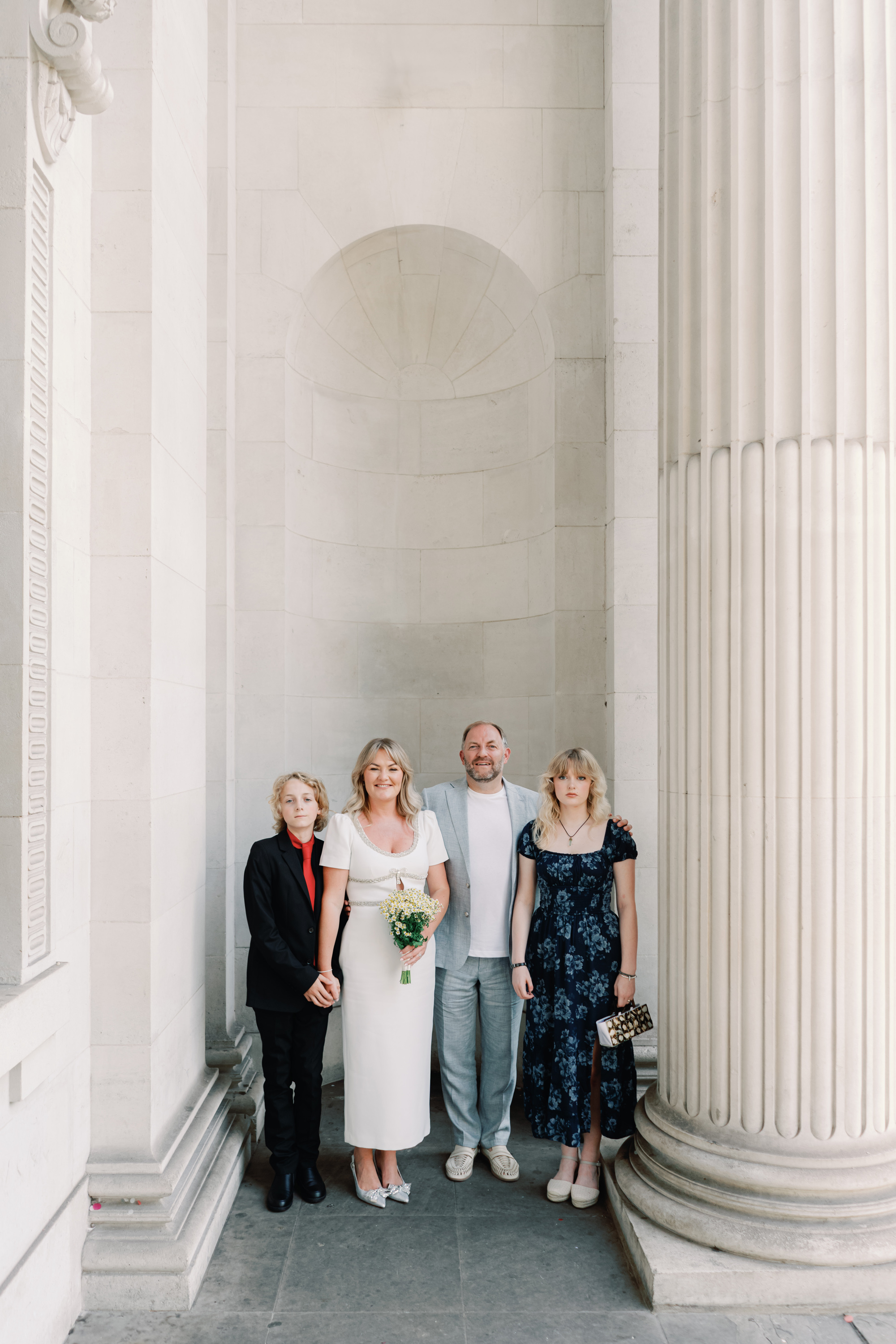 Emmylou Kelly Registry Office Wedding Jessica Lily Photography 118 - Photographer Emmylou Kelly & Paul's Intimate Family Registry Office Wedding Bride and groom standing with their son and daughter by the tall pillars outside Old Marylebone Town Hall