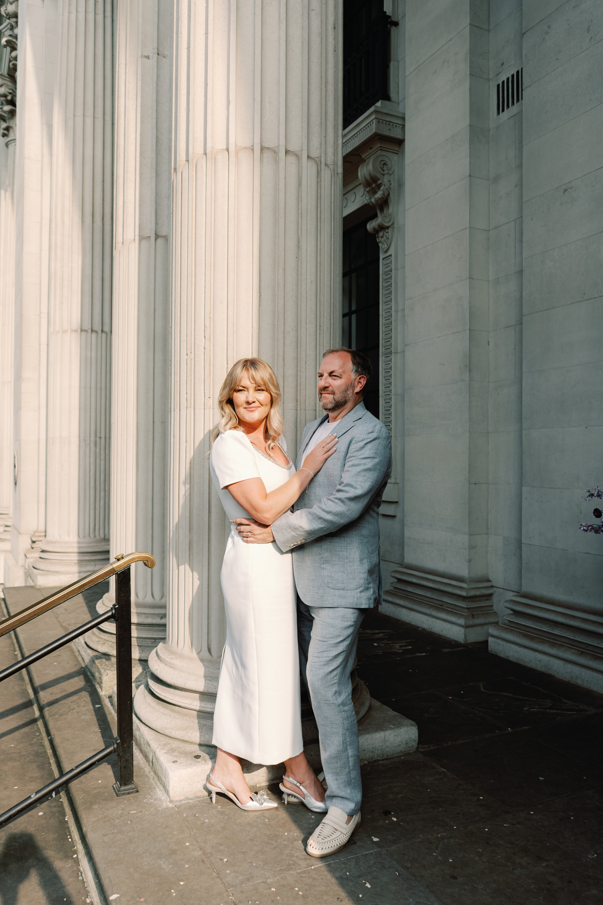 Emmylou Kelly and her husband Paul. The bride wears a dress by Self Portrait and carries a small bouquet of Feverfew. The groom wears a relaxed pale blue suit by Moss Bros.