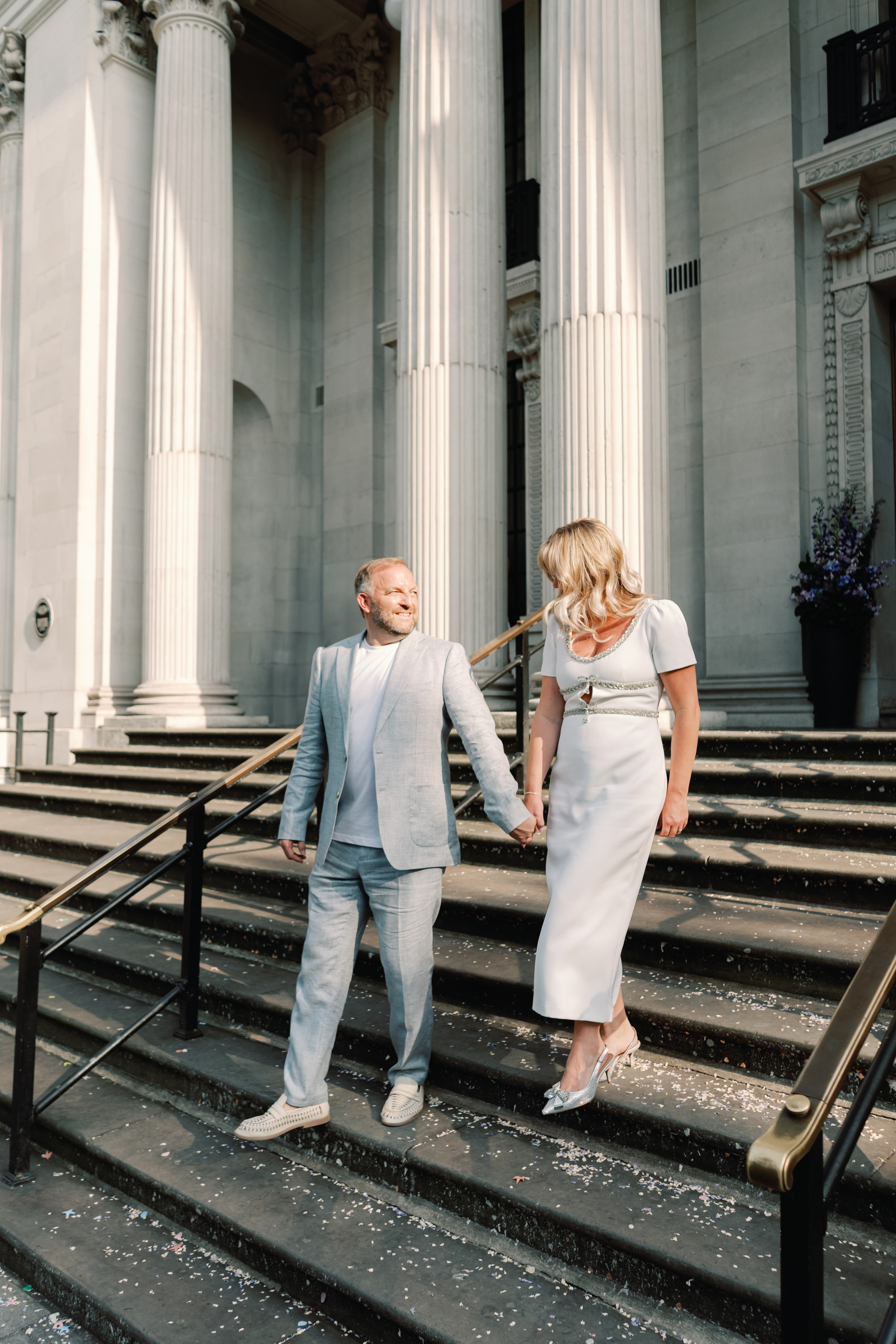 Emmylou Kelly Registry Office Wedding Jessica Lily Photography 126 - Photographer Emmylou Kelly & Paul's Intimate Family Registry Office Wedding Groom in pale blue suit and white tshirt holding the hand of his bride in a midi dress by Self Portrait as the descent the stairs at Old Marylebone Town Hall on their wedding day.