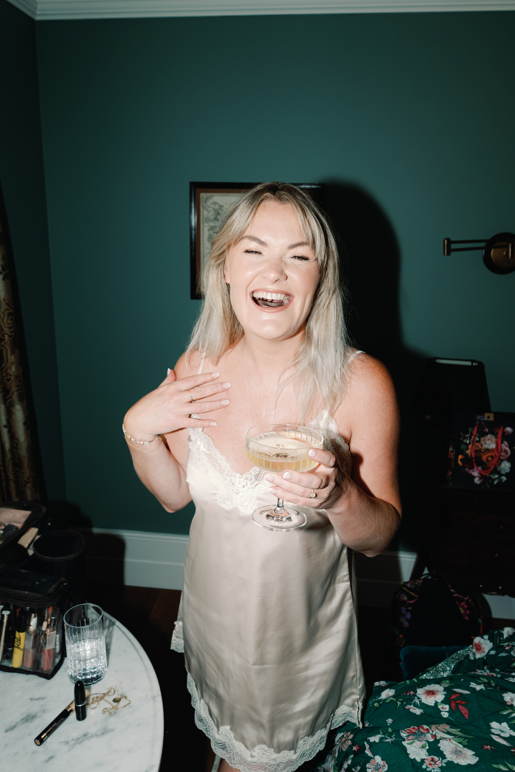 Bride in a silk slip as she gets ready on the morning of her wedding. She is sipping from a champagne coupe.