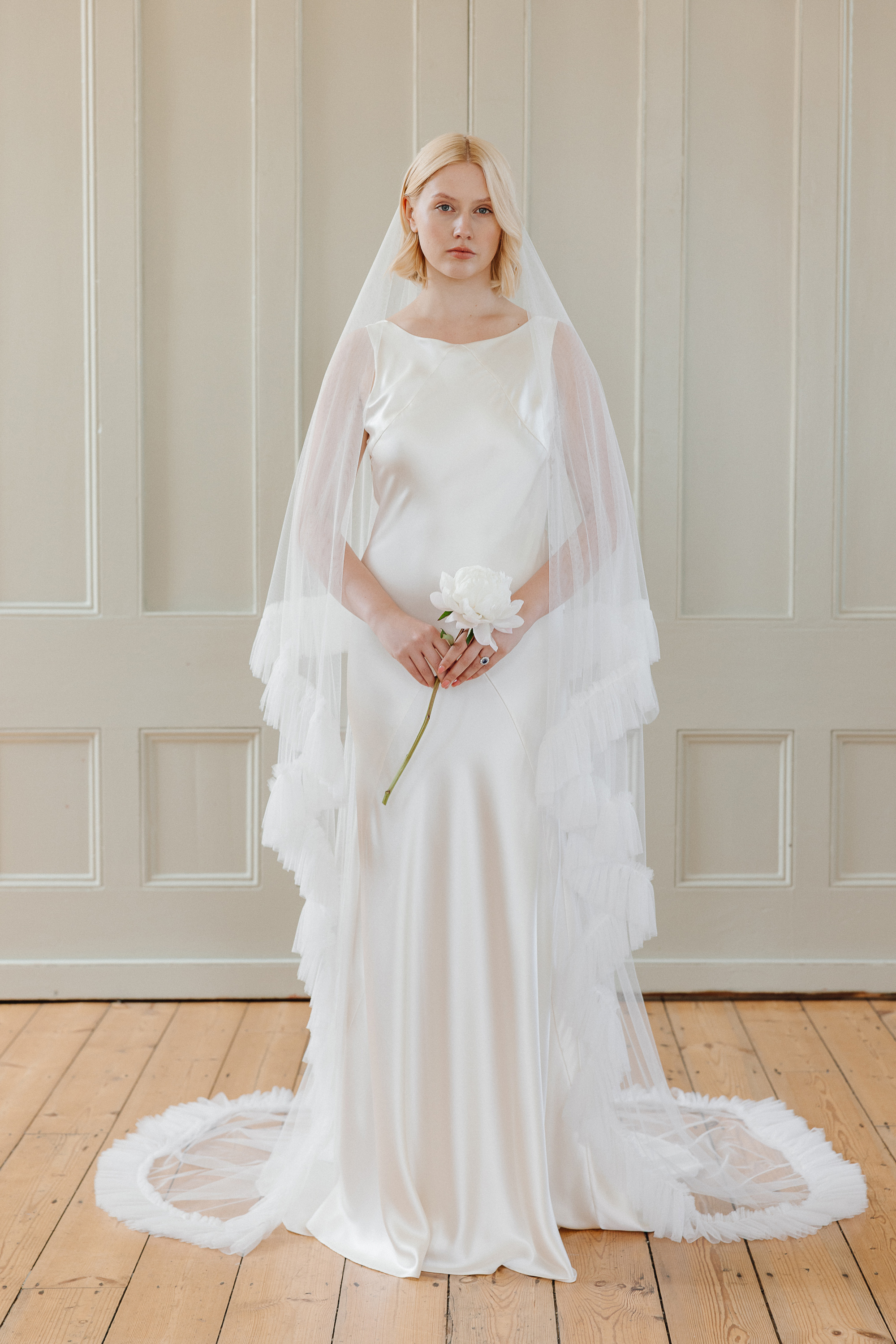 Gladioli cowl back bias cut silk wedding gown KateBeaumont Icons 2 IndiaHobson HR 223 - Kate Beaumont: Lovingly Handmade Silk Wedding Dresses Model bride holding a single stem rose and wearing a Kae Beaumont wedding dress and veil with tassel fringed hem.