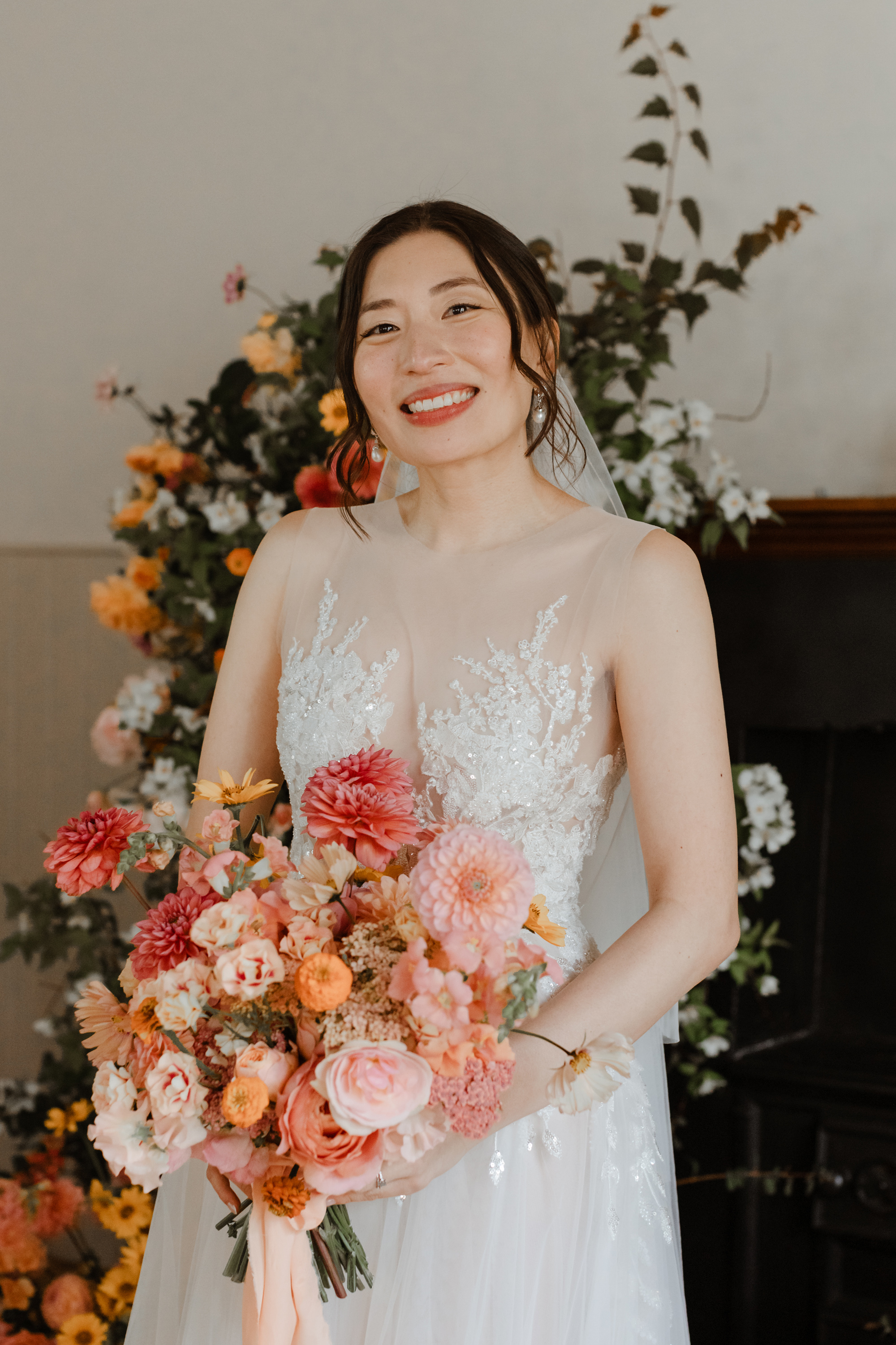 Asian bride with beautiful natural wedding day makeup, and carrying a large colourful summer bouquet with peach silk ribbons.