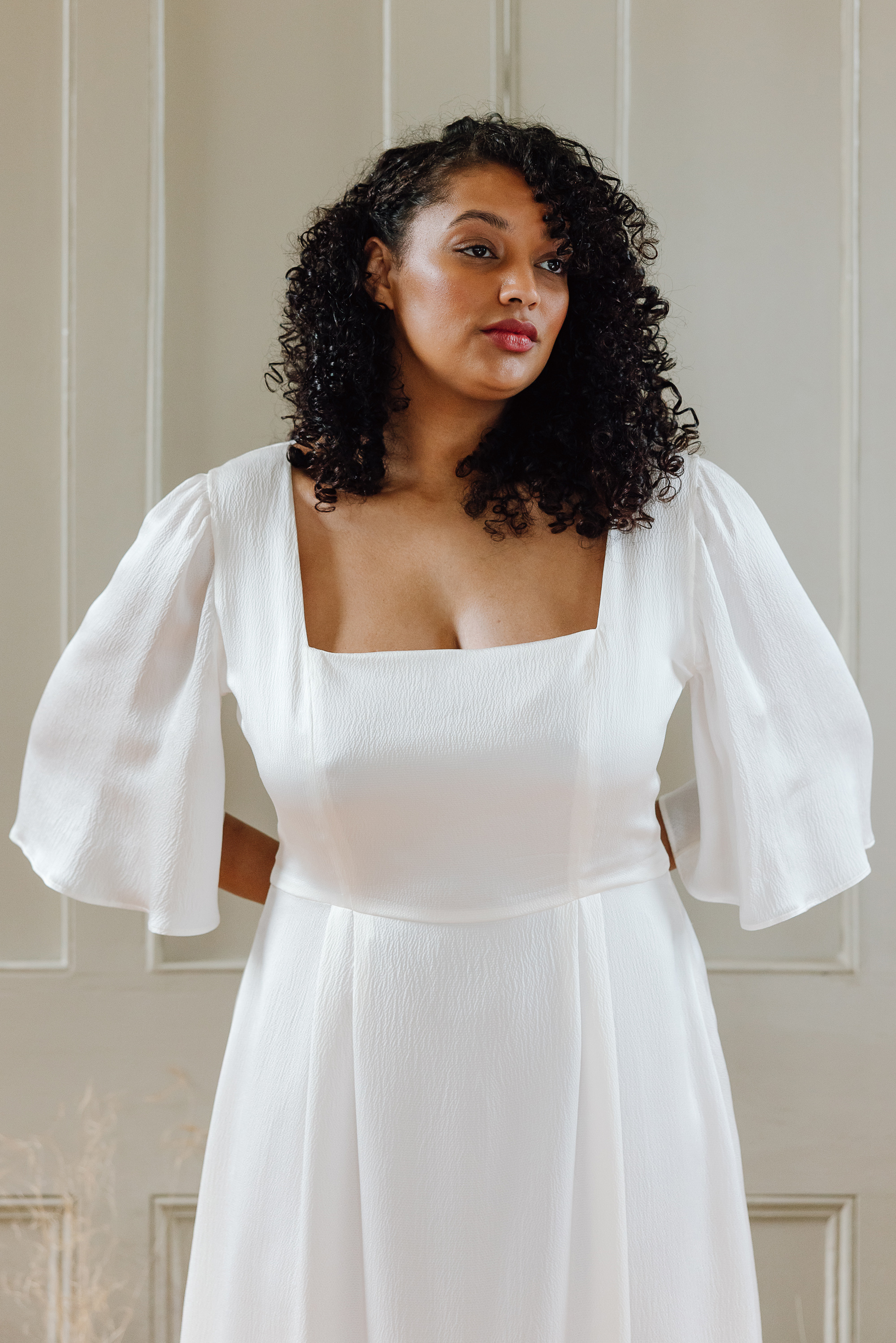 Black curvy bride with loose curly hair, wearing a modern bridal gown by Kate Beaumont.