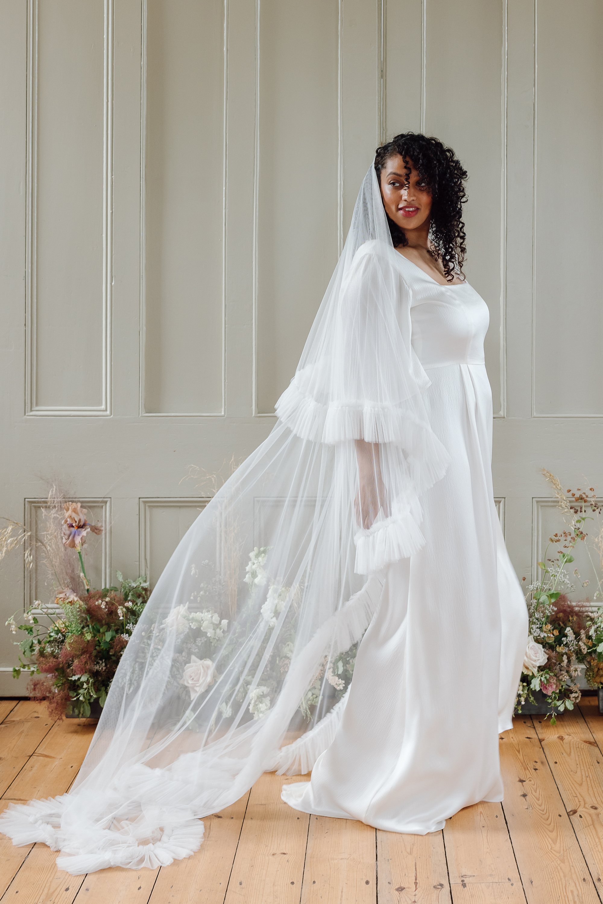 Black curvy bride with loose curly hair, wearing a modern bridal gown by Kate Beaumont.