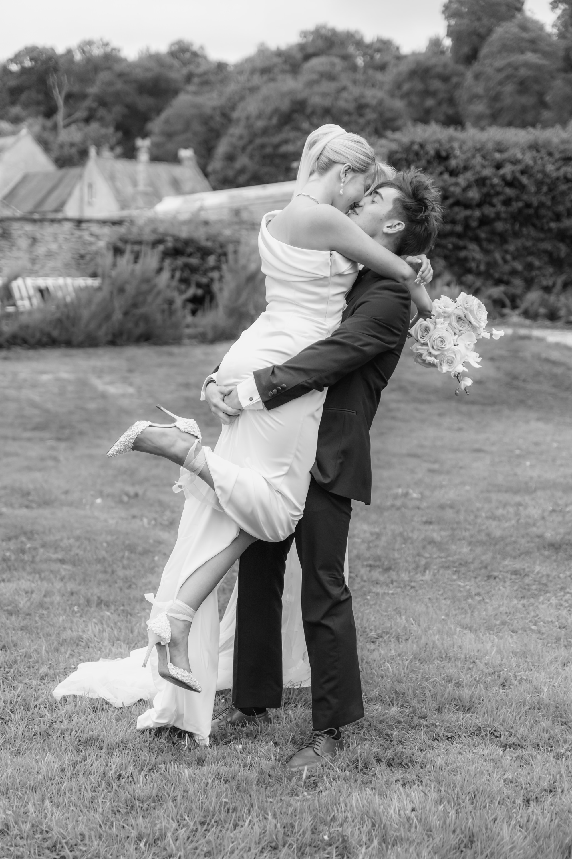 Relaxed Romance, A Pastel Wedding Editorial at Newton Surmaville in Somerset 41 Groom in black tie lifting his bride in the air, they are kissing as he does so. She wears Wona Concept dress and Di Hassall shoes.