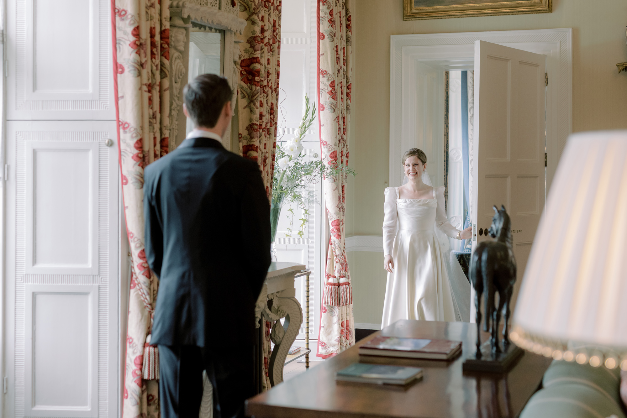 Groom looking ahead to his bride in a Phillipa Lepley wedding dress as she opens the door to reveal herself during a first look.