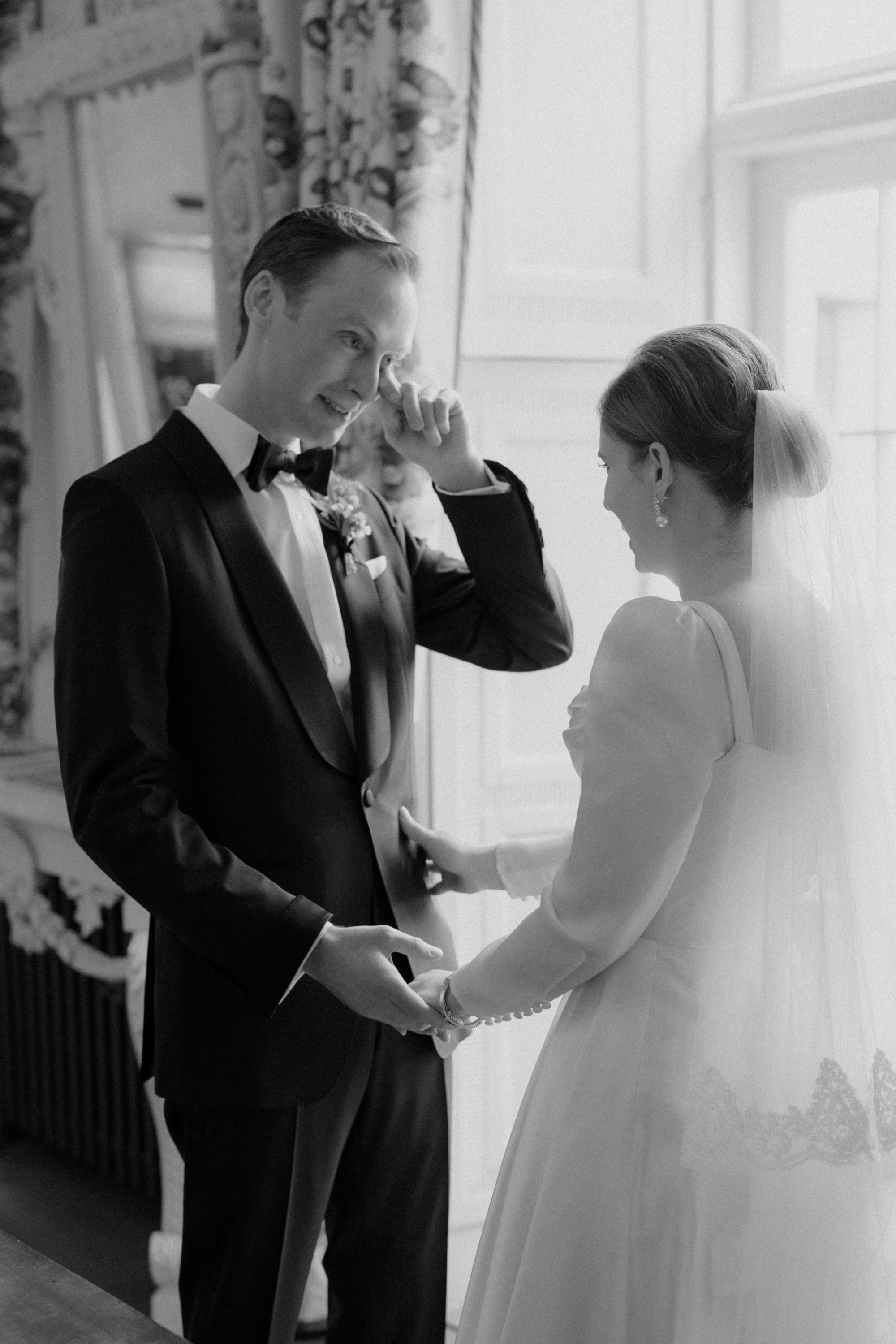 Groom in black tie wiping a tear from his eye during a first look.