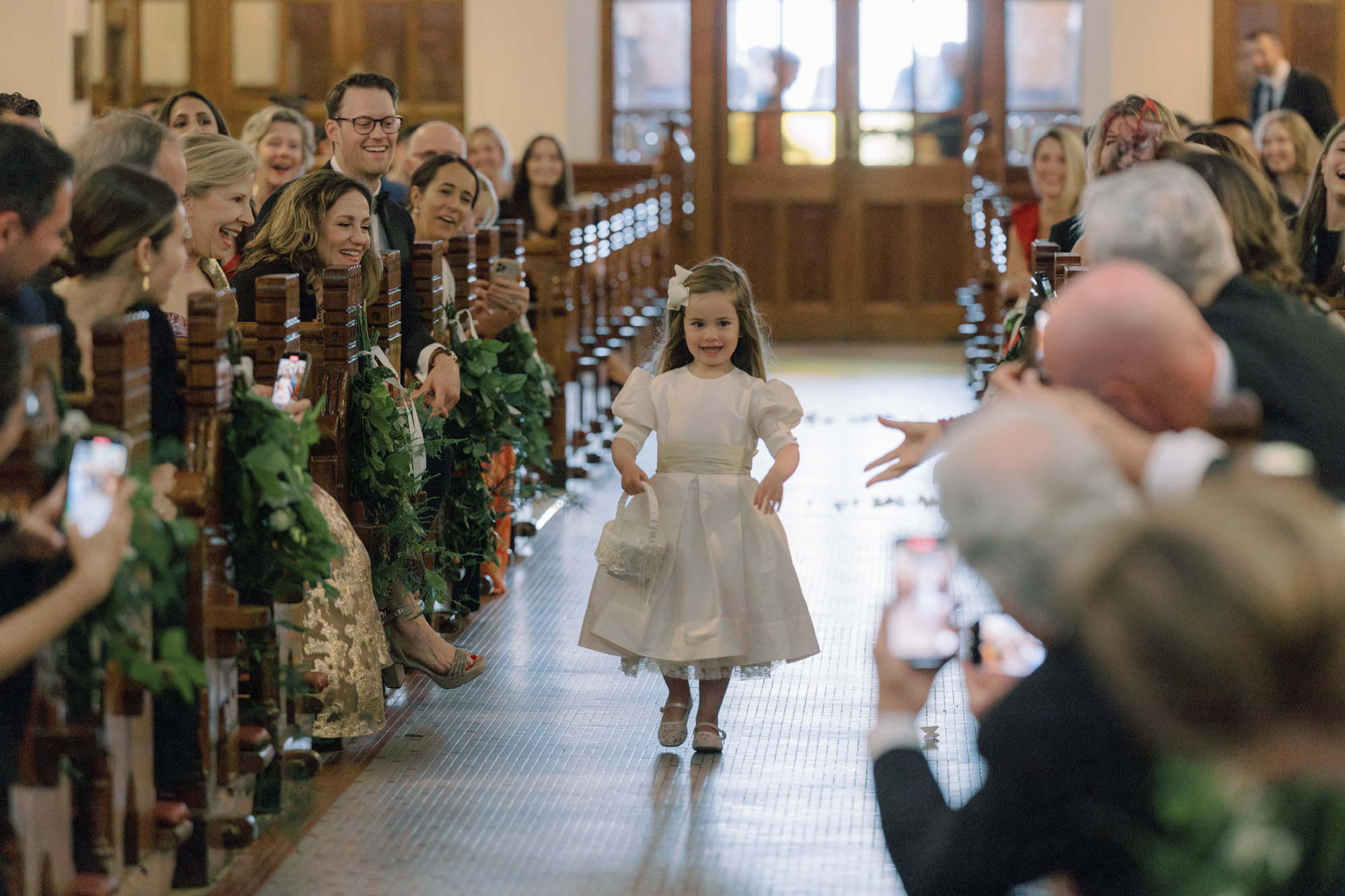 Sweet flower girl wearing a traditional flower girl dress and carrying a basket of petals, walking down the aisle at a wedding.