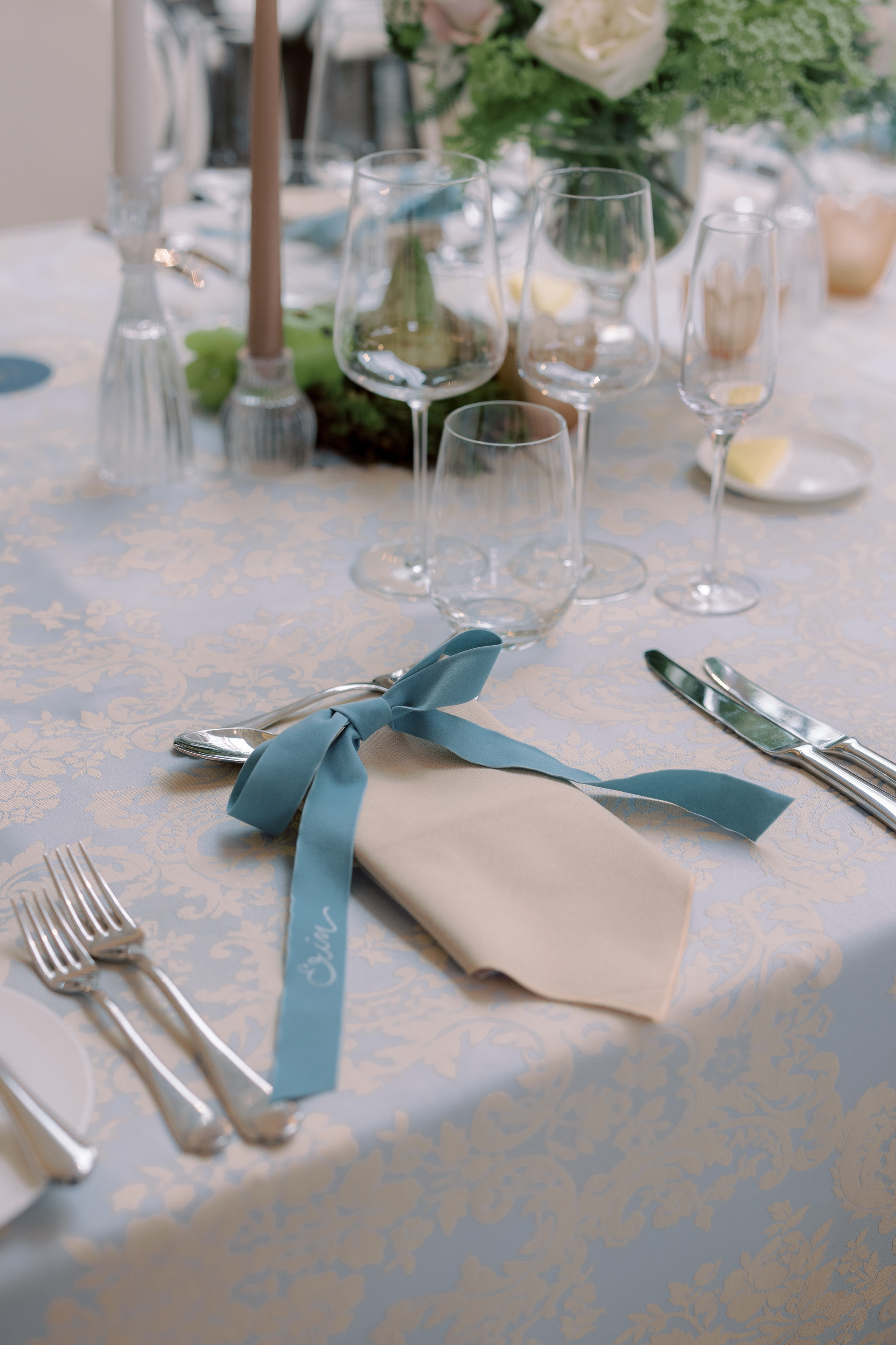 Embroidered pale blue ribbon resting on top of a napkin at a wedding reception.