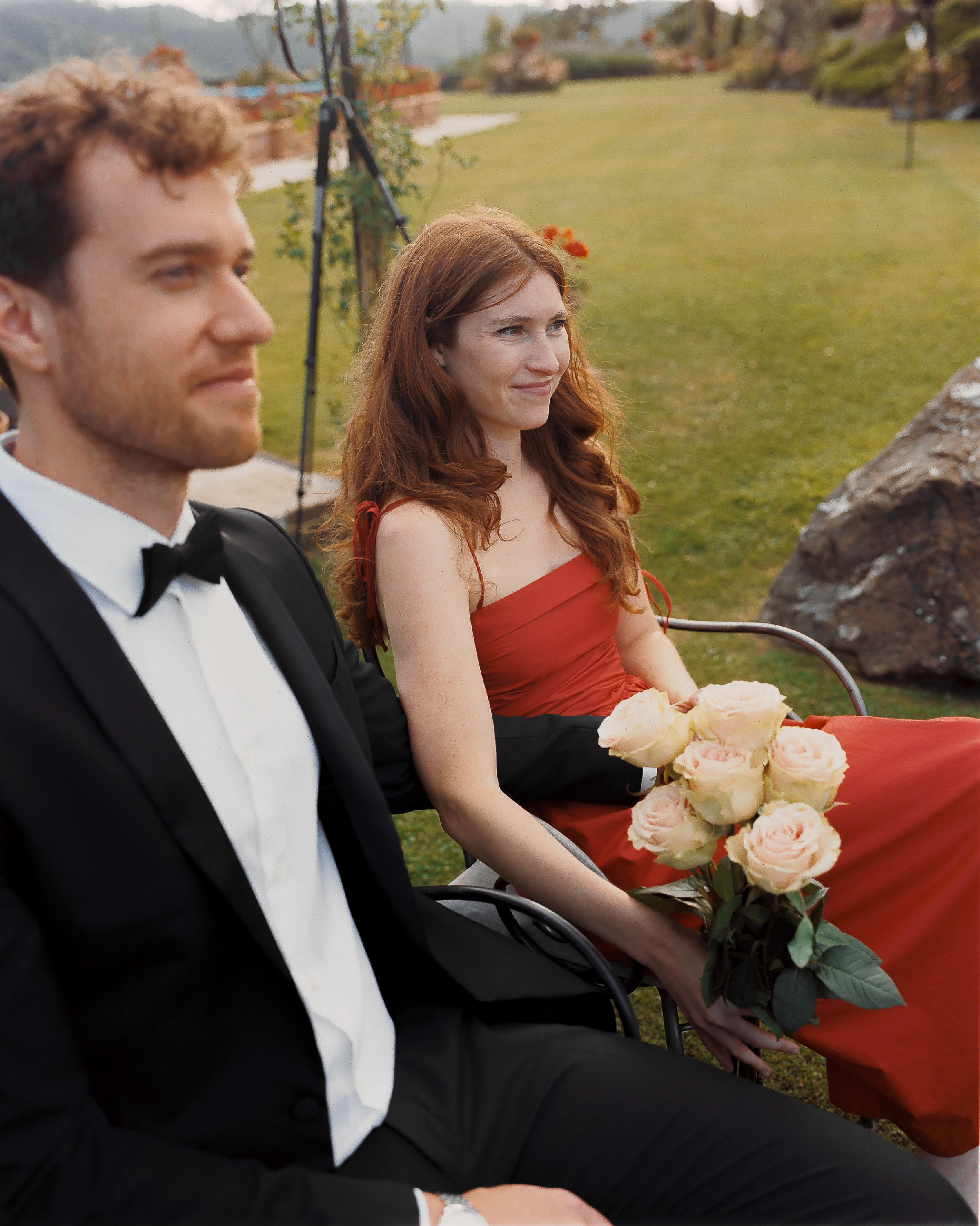 Romantic Tuscan Elopement on Film 130 - An Original 1940s Vintage Dress for Emily & Ned's Intimate Elopement in Tuscany Wedding guest and bridesmaids wears a red dress as she is seated next to the groomsman in black tie. Outdoor ceremony in the gardens of an Italian villa.