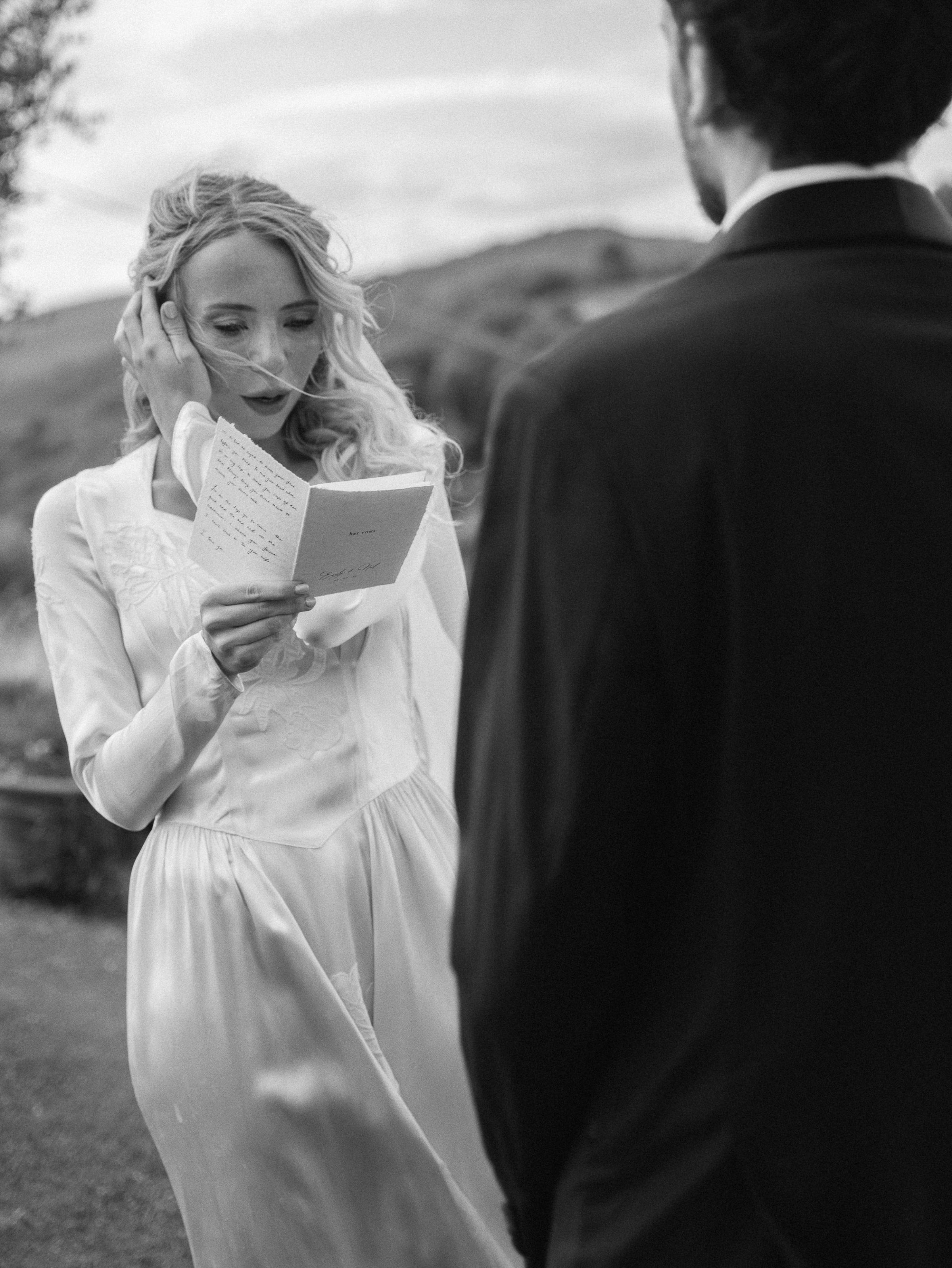 Romantic Tuscan Elopement on Film 133 - An Original 1940s Vintage Dress for Emily & Ned's Intimate Elopement in Tuscany Emotional bride reading her vows from a booklet during the outdoor ceremony in Tuscany. She wears an original 1940's vintage silk wedding dress and is using her hand to keep the breeze from gently blowing hair into her face. Tender moment of emotion during the elopement ceremony.