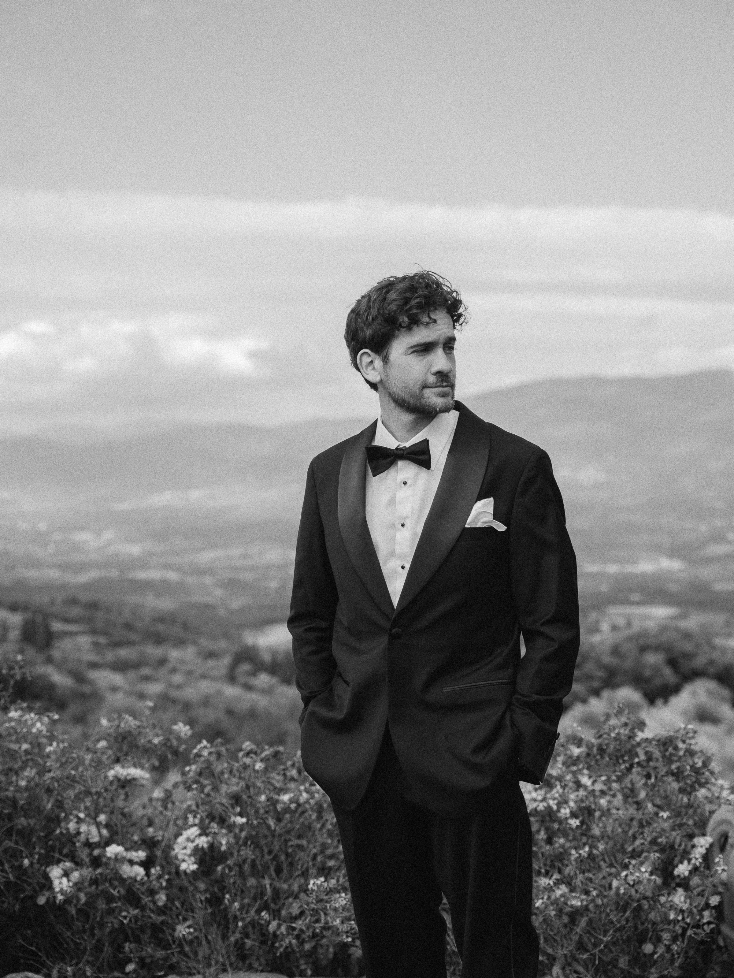 Romantic Tuscan Elopement on Film 92 - An Original 1940s Vintage Dress for Emily & Ned's Intimate Elopement in Tuscany Groom in black tie standing outdoors waiting for his bride - the Tuscan hills in the background.