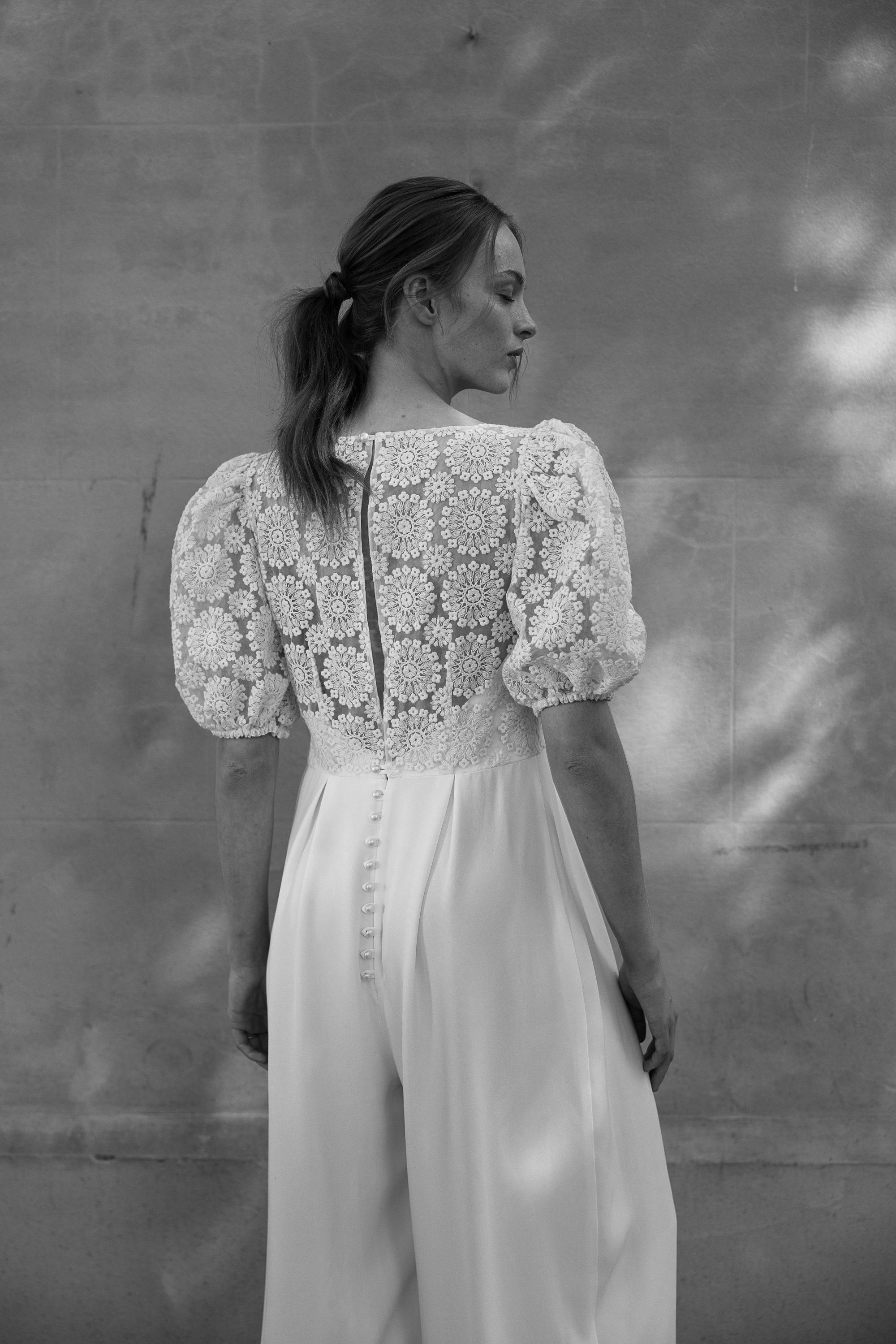 Viburnum silk bridal jumpsuit KateBeaumont 2025 IndiaHobson HR 335 - Kate Beaumont: Lovingly Handmade Silk Wedding Dresses Black and white shot of the back of a bride wearing a silk and floral lace wedding jumpsuit.