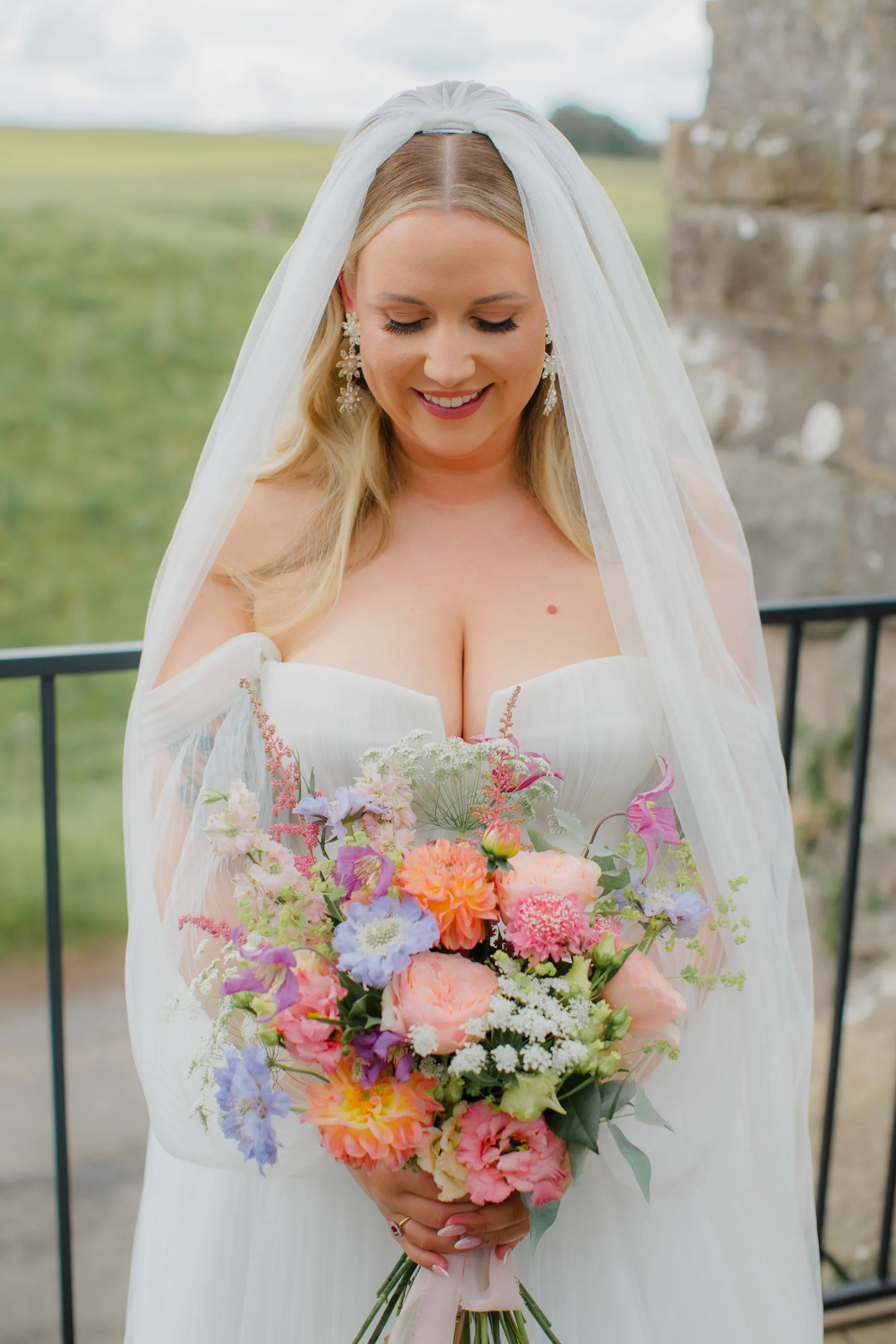 Colouful Folkerton Mill Wedding Lanark Scotland 224 - A Colourful, Relaxed Family Wedding at Folkerton Mill in Lanark, Scotland Bridal portrait, bride looks down on her elegant and colourful summer bouquet. She wears a Lena Leena wedding dress, starry earrings and a long veil that falls from the top of her head.
