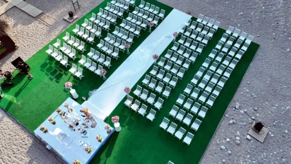 Alt Text: Aerial drone view of Persian Sofreh Aghd wedding ceremony setup on beach with white chairs and aisle in Antalya Turkey by Ramarossi