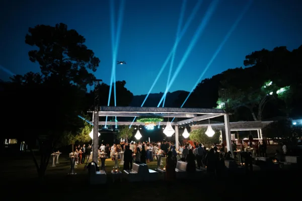 Outdoor wedding party with dramatic searchlight beams crystal chandeliers and guests mingling at night venue in Antalya Turkey by Ramarossi