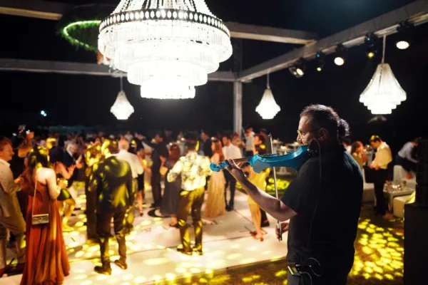 Electric violinist performing at wedding party with guests dancing under crystal chandeliers and spotlight patterns on dance floor in Antalya Turkey by Ramarossi