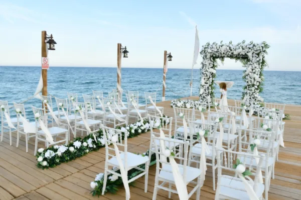 Wedding ceremony setup on wooden beach pier with white floral arch chiavari chairs and Mediterranean Sea view in Antalya Turkey by Ramarossi