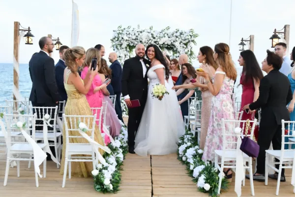 Bride and groom walking down aisle at intimate Lebanese wedding ceremony on beach pier with white floral arch and Mediterranean Sea in Antalya Turkey by Ramarossi