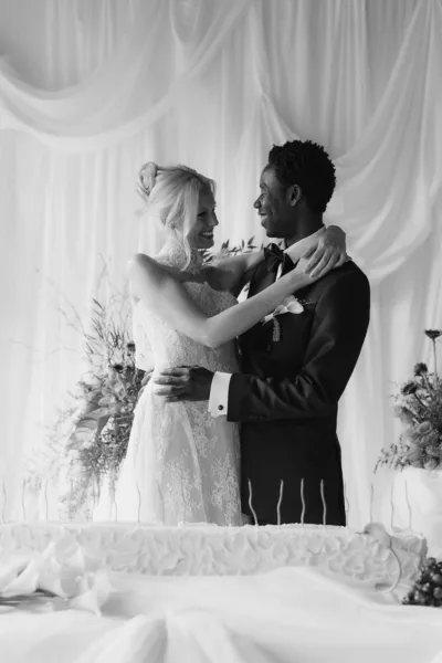 Black and white wedding portrait of bride and groom embracing beside their wedding cake at Iscoyd Park in Shropshire, captured in an editorial style by Cleo Stella Photography.